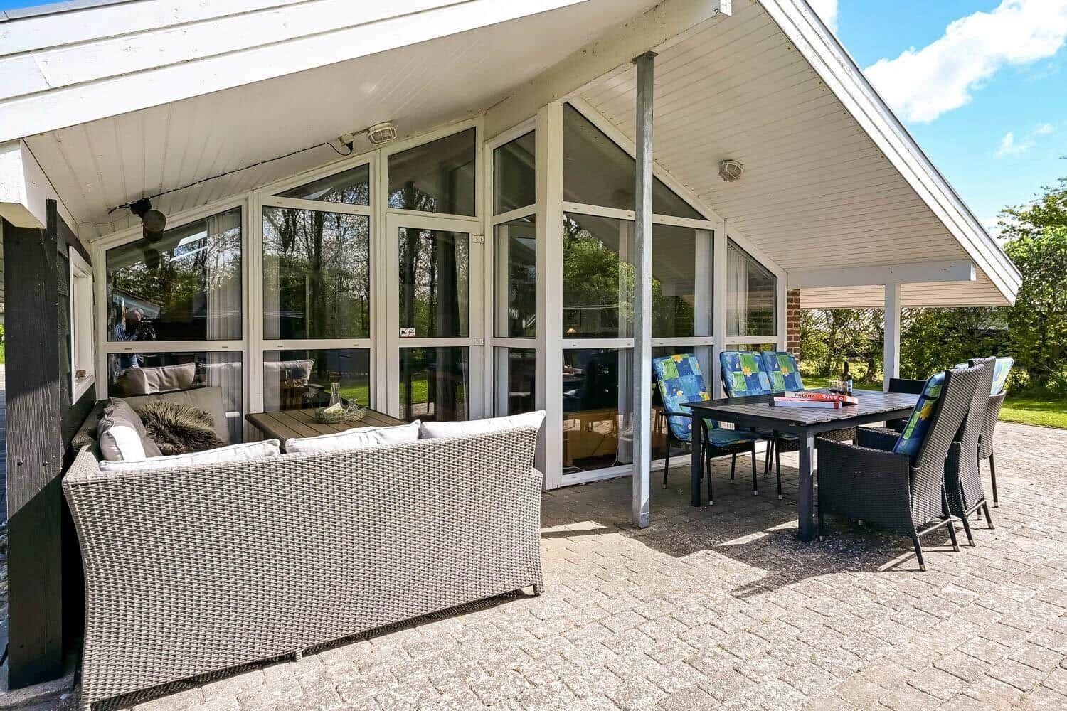 Terrace with seating area and dining table under a roof. Large window front to the apartment.