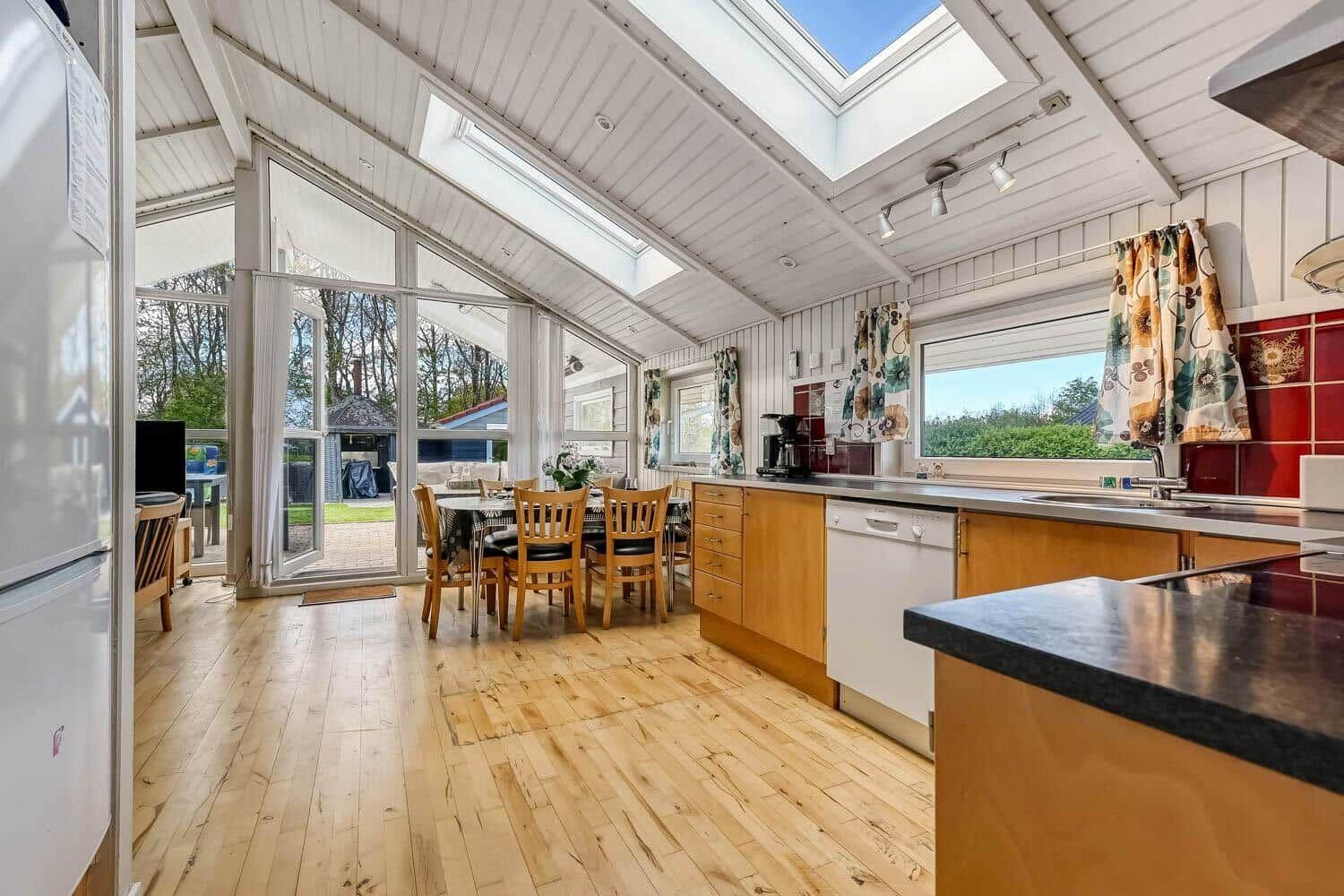 Kitchen with dining area, wooden floor, and skylights. View of garden through glass doors.