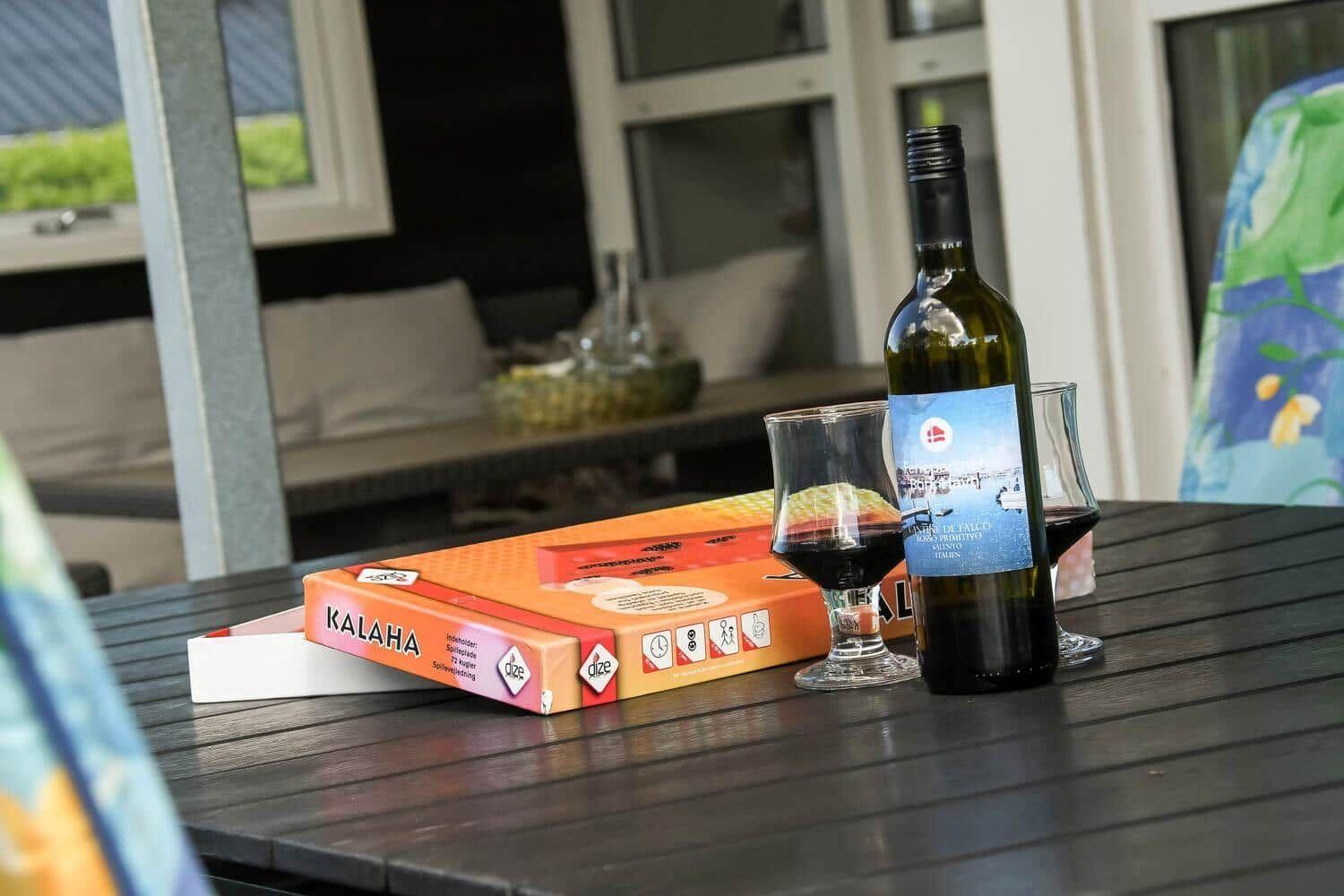 On the table are a wine bottle, two glasses, and the board game Kalaha.