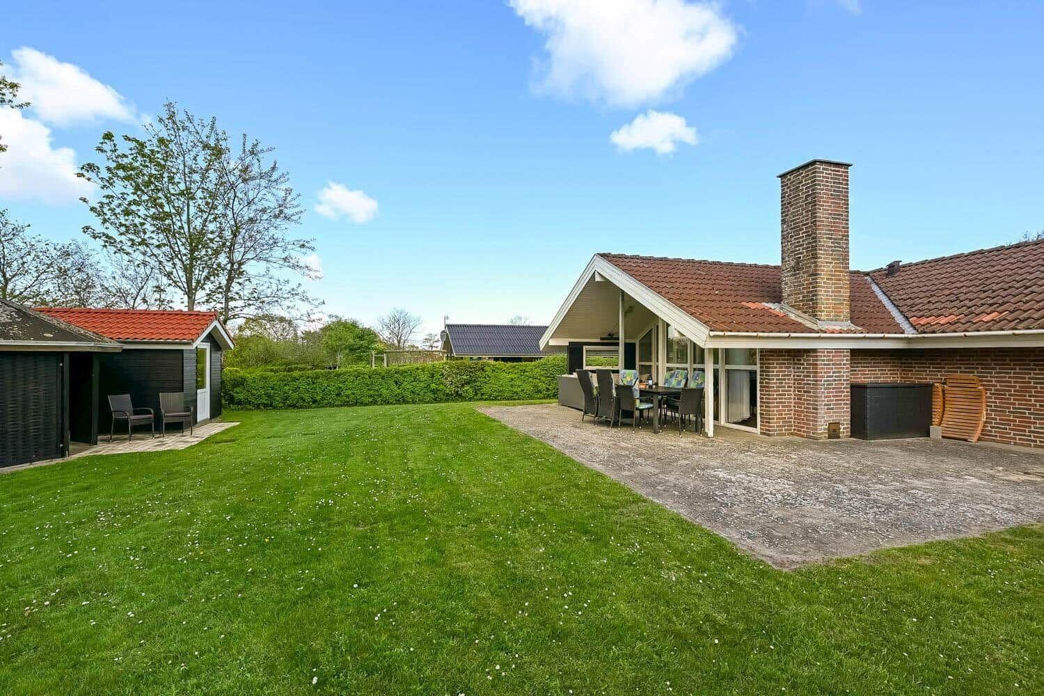 House with garden, terrace, and grill area under blue sky.