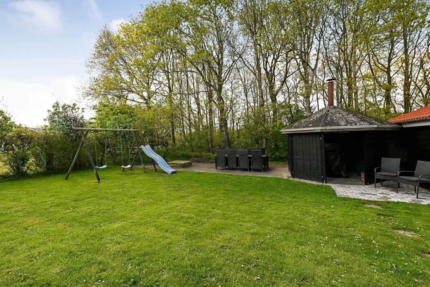 Backyard with playground, grill house, and seating. Lawn and trees in the background.