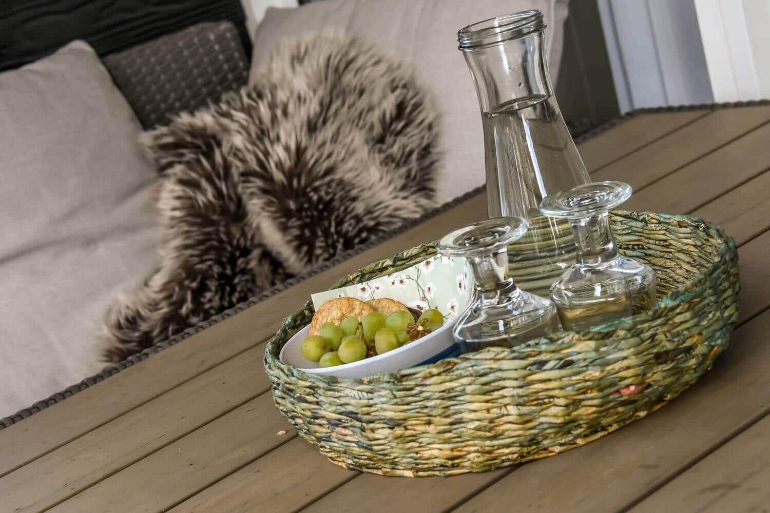 A tray with wine, grapes, and bread sits on the table. In the background, a sofa with a fur blanket.