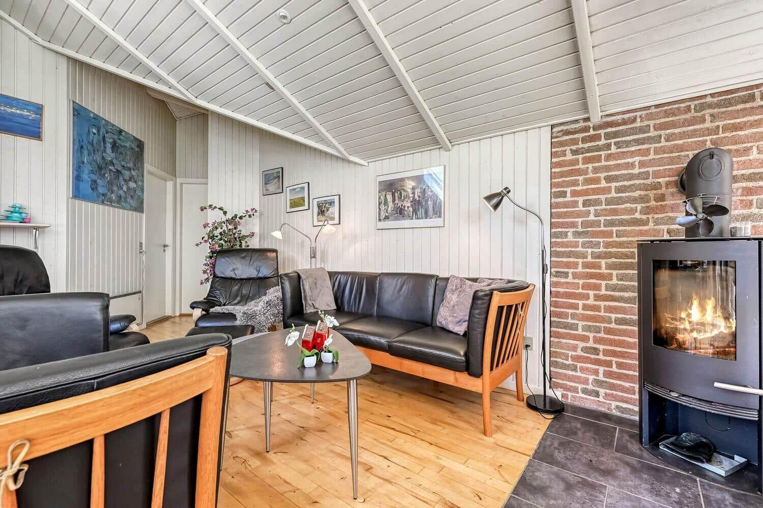 Living room with sofa, armchairs, and wood-burning stove against brick wall.