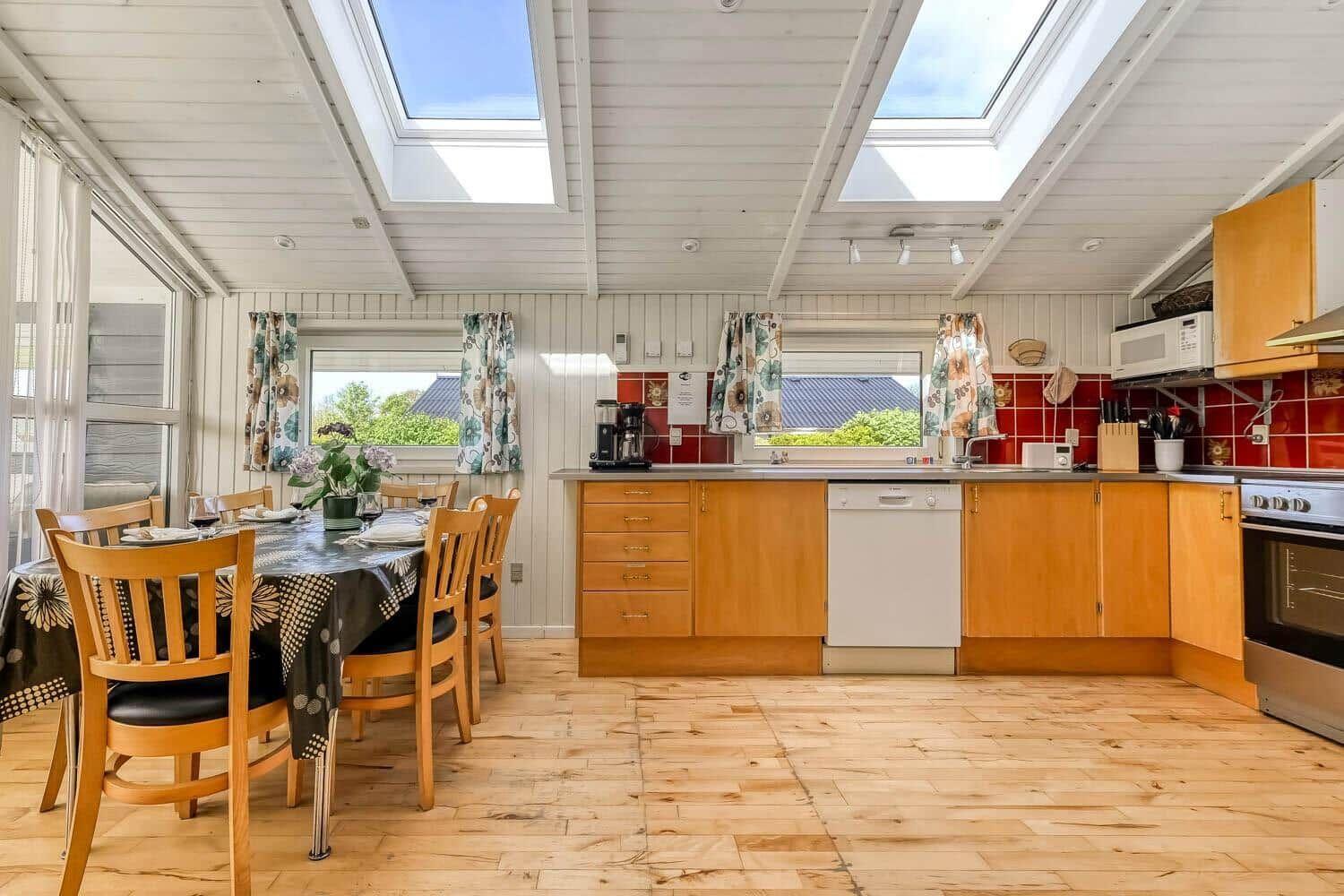 Kitchen with dining area, wooden floor, and skylights. Red tiles and wooden cabinets.