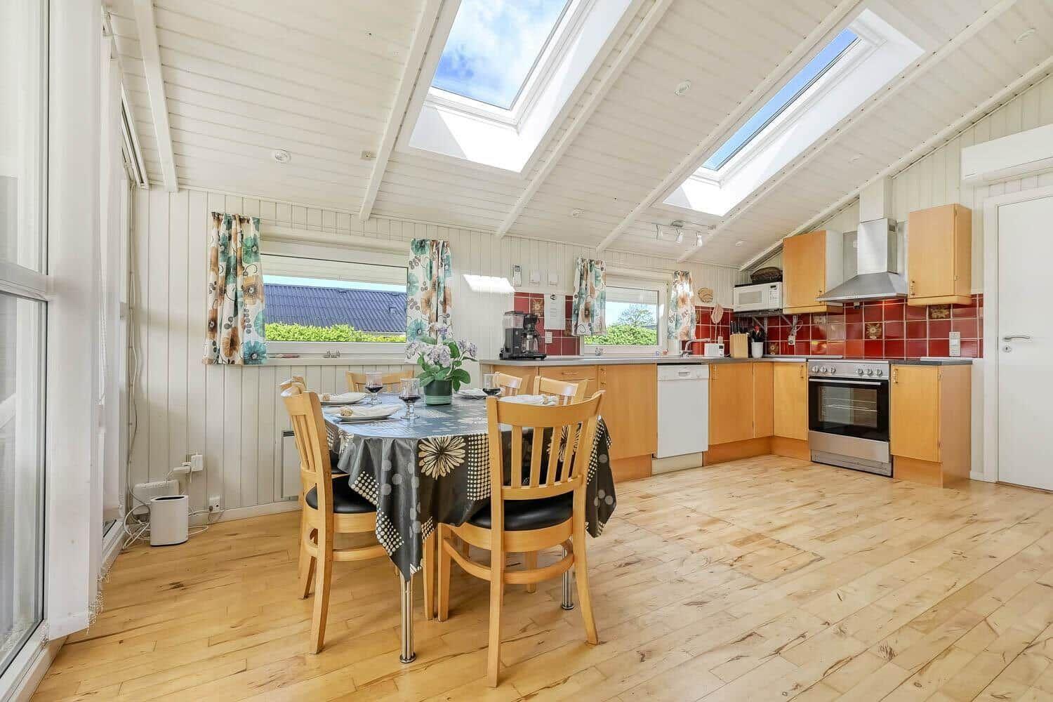 Kitchen with dining area, wooden floor, and skylights. Red tiled wall and wooden cabinets.