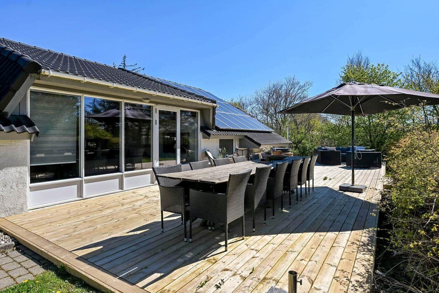 Terrasse mit Tisch, Stühlen und Sonnenschutz. Haus mit großem Fensterbereich und Solaranlage.