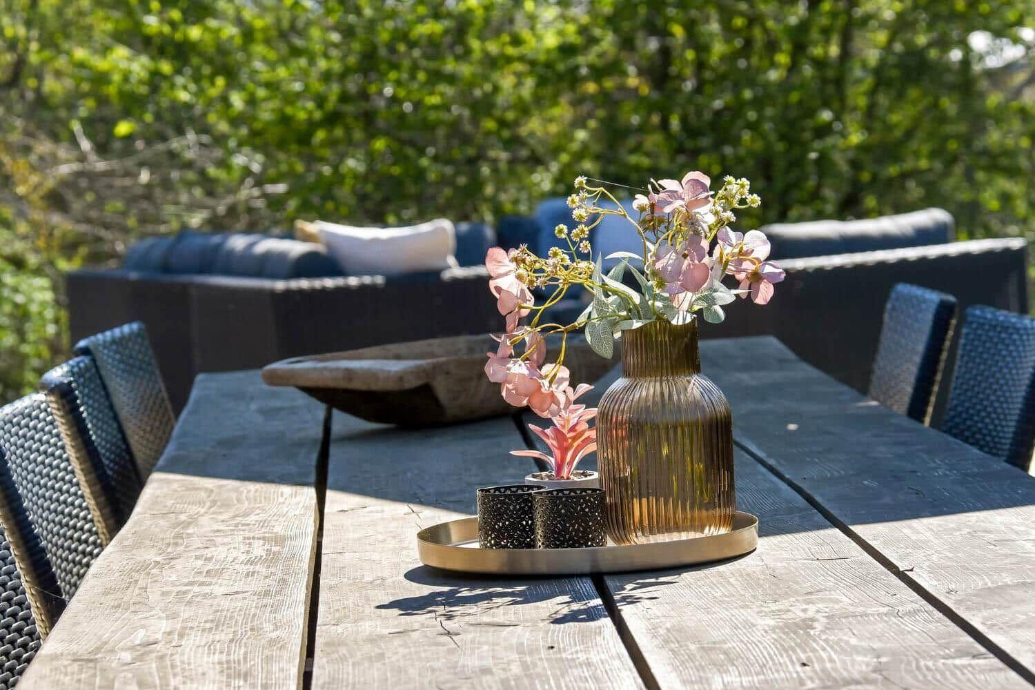 Holztisch mit Blumenvase und Stühlen im Garten
