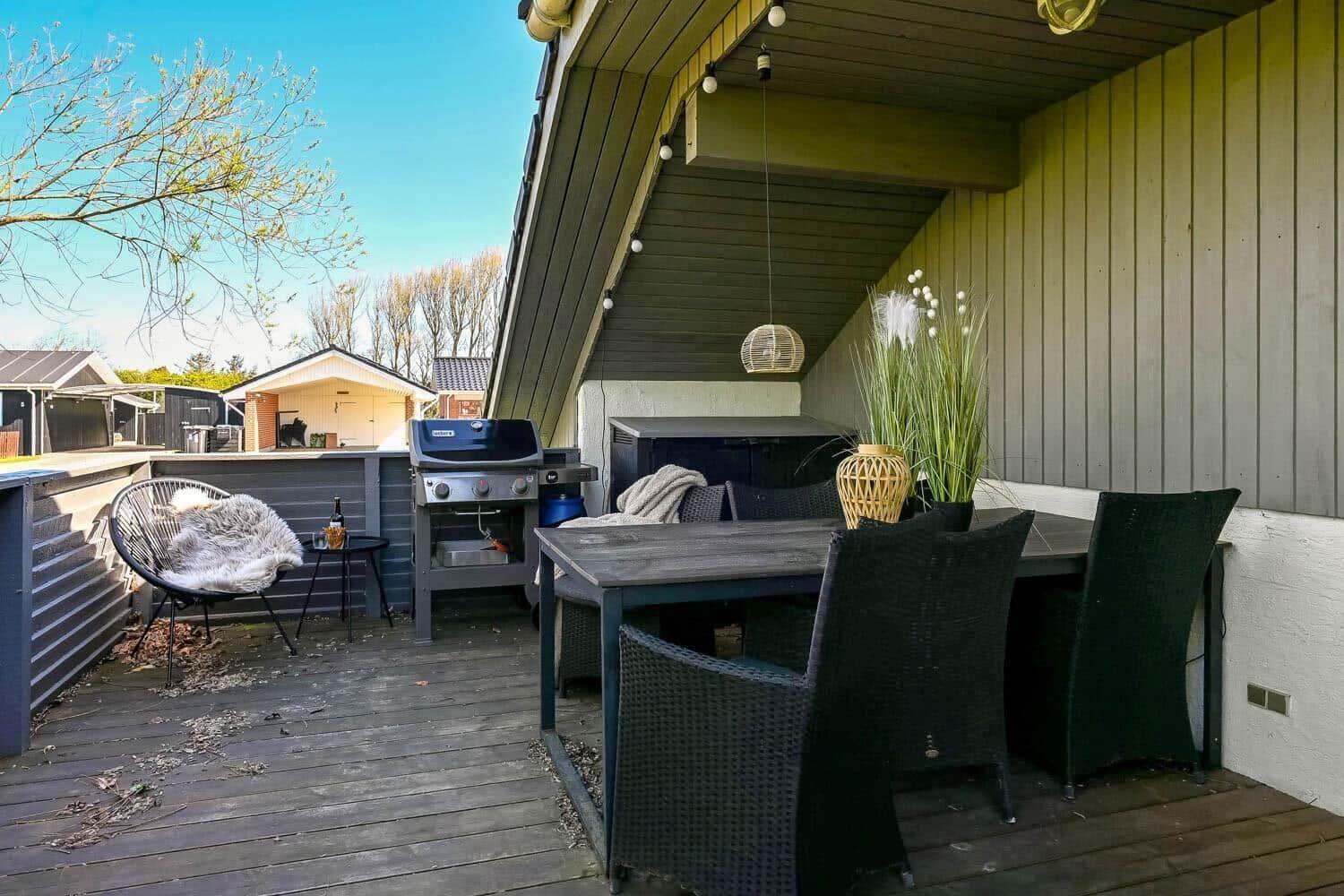 Terrasse mit Tisch, Stühlen, Grill und Pflanze unter Holzverkleidung.
