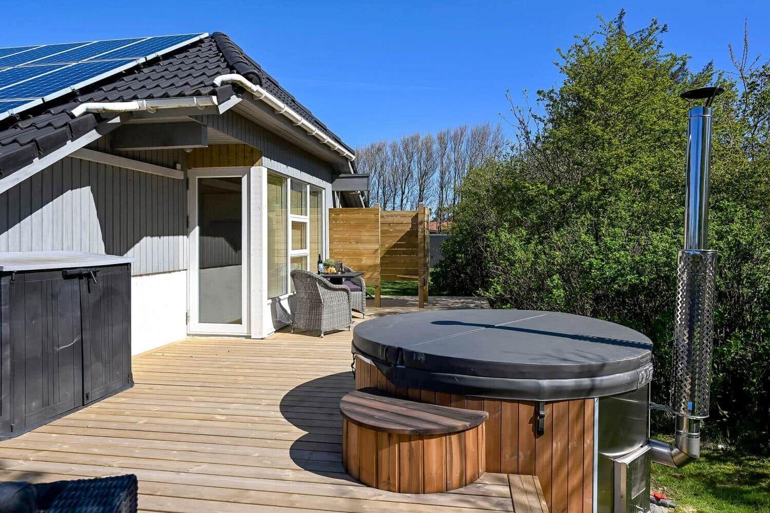 Hütte mit Holzterrasse, Whirlpool und Solaranlage. Garten mit Bäumen und Sitzgelegenheiten.
