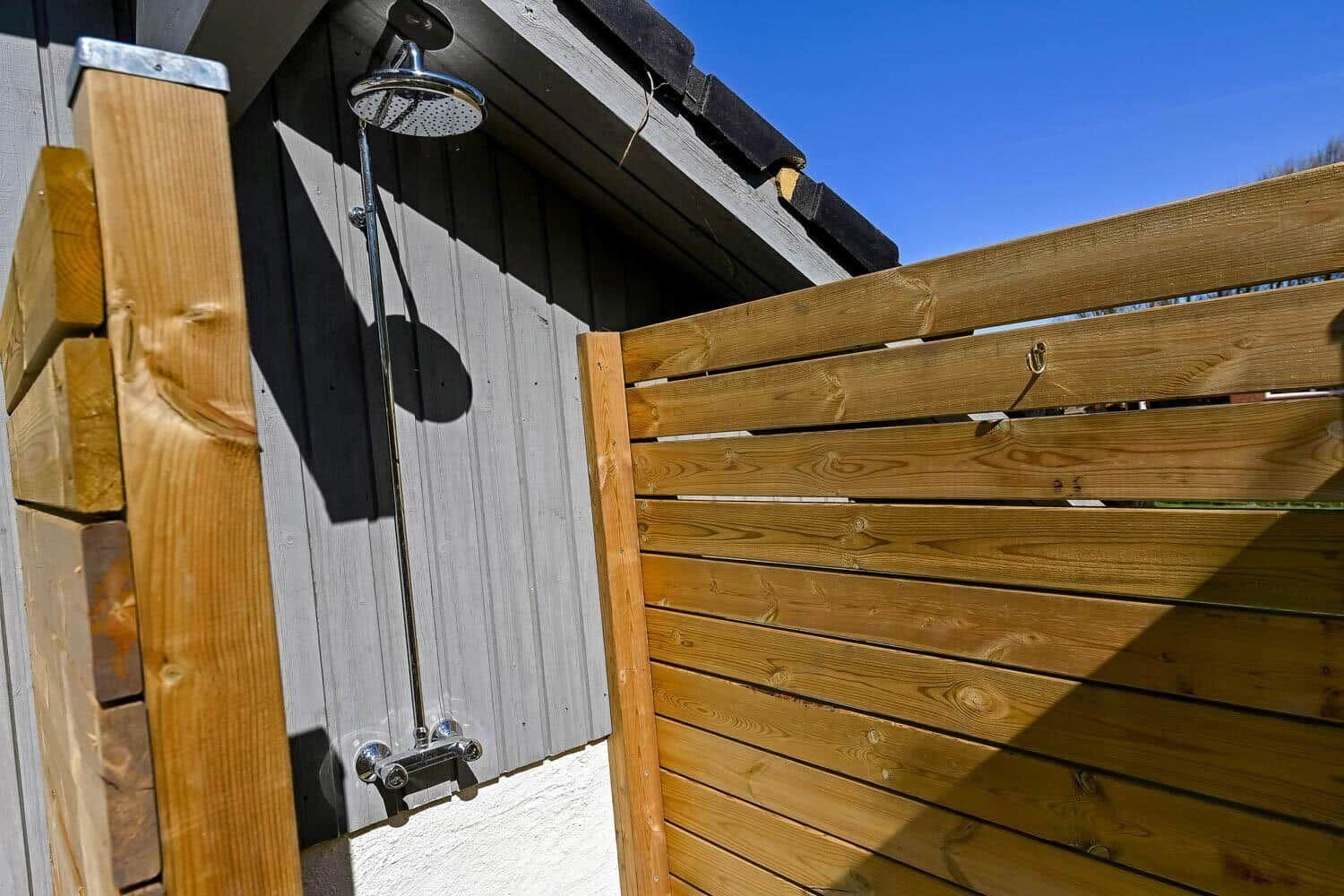 Außen-Dusche mit Duschbrause an Holzwand unter Dach