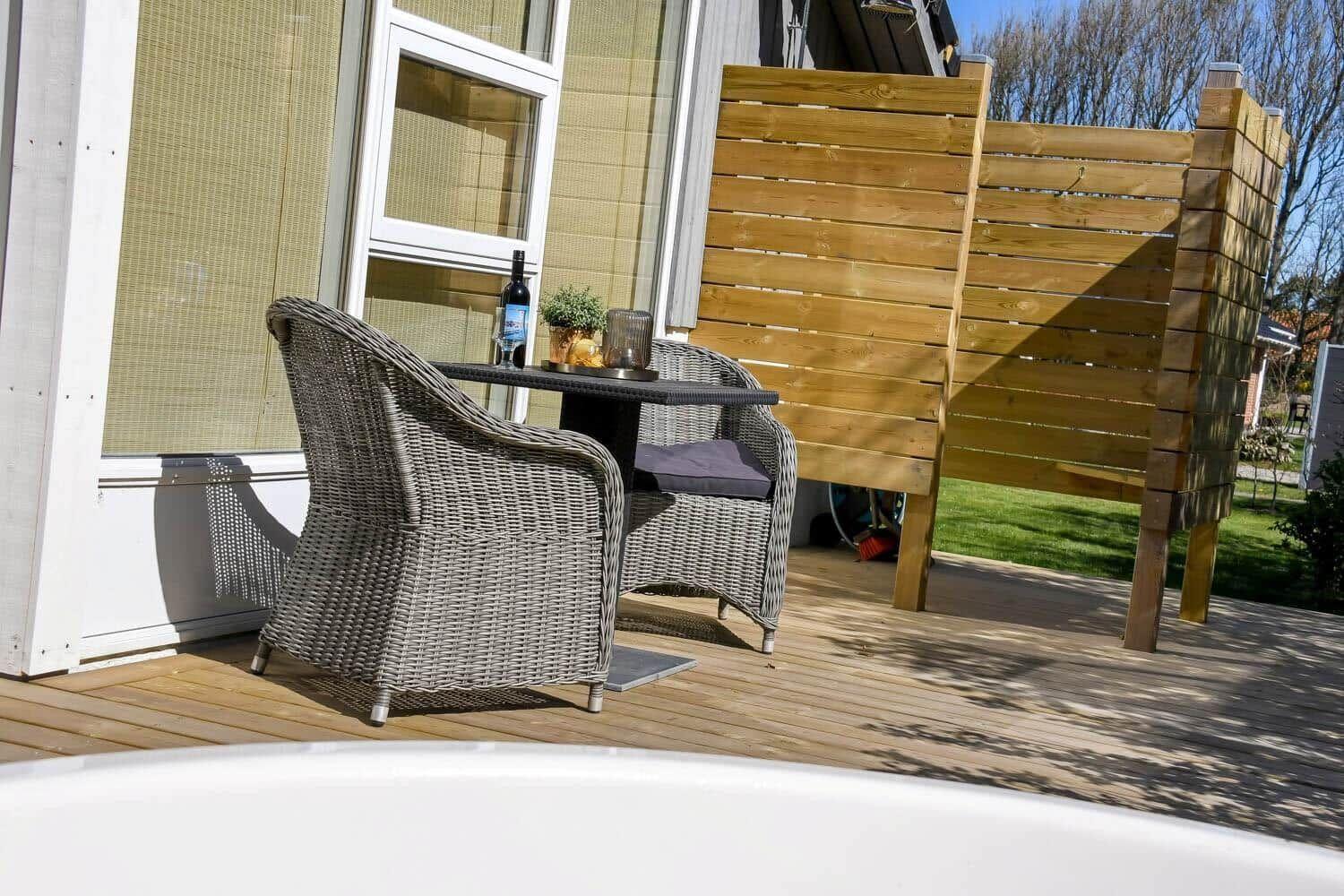 Terrasse mit zwei Stühlen und Tisch. Hintergrund: Holzgeländer und Hauswand.