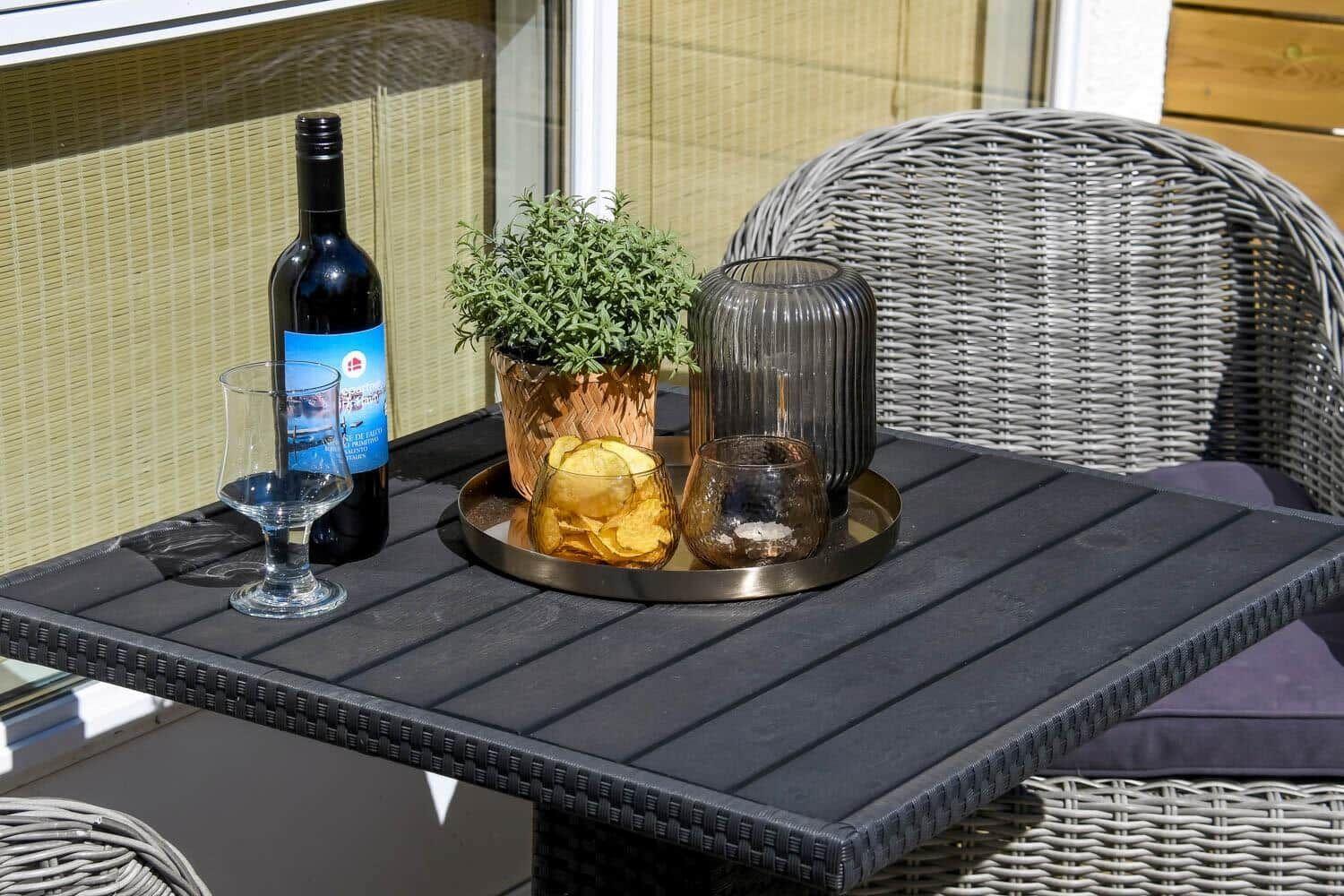 Schwarzer Tisch mit Weinflasche, Gläsern und Pflanze im Freien.