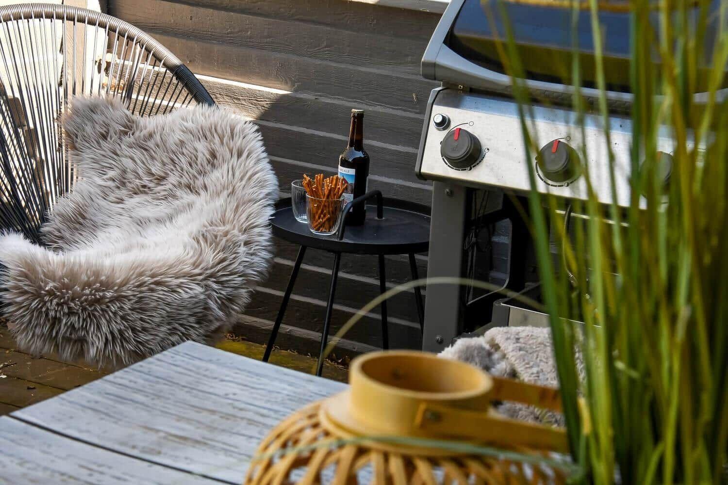 Außenbereich mit Grill, Stuhl und Tisch. Auf dem Tisch stehen Getränke und Snacks.