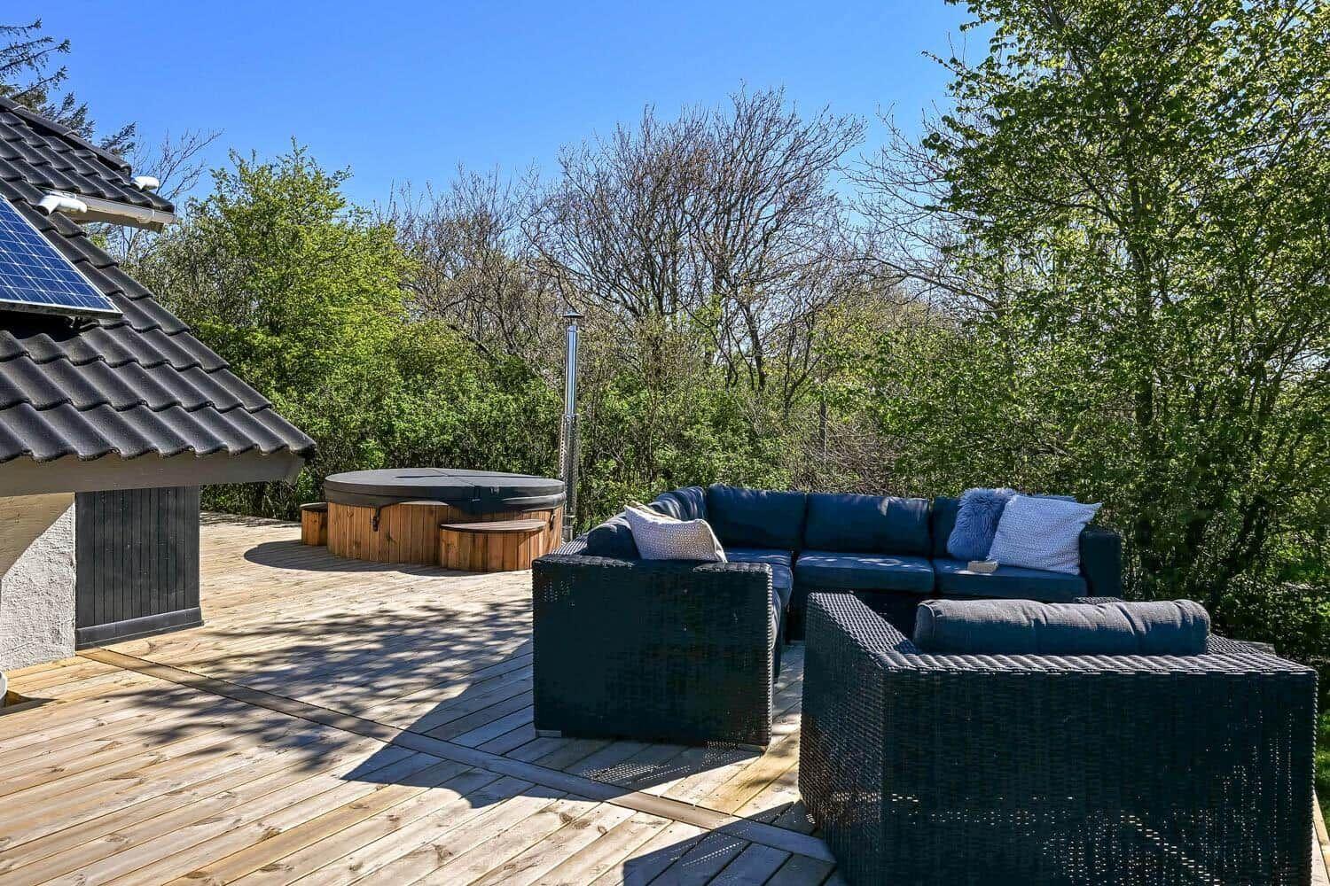Terrasse mit Hot Tub und Sitzgruppe umgeben von Bäumen.