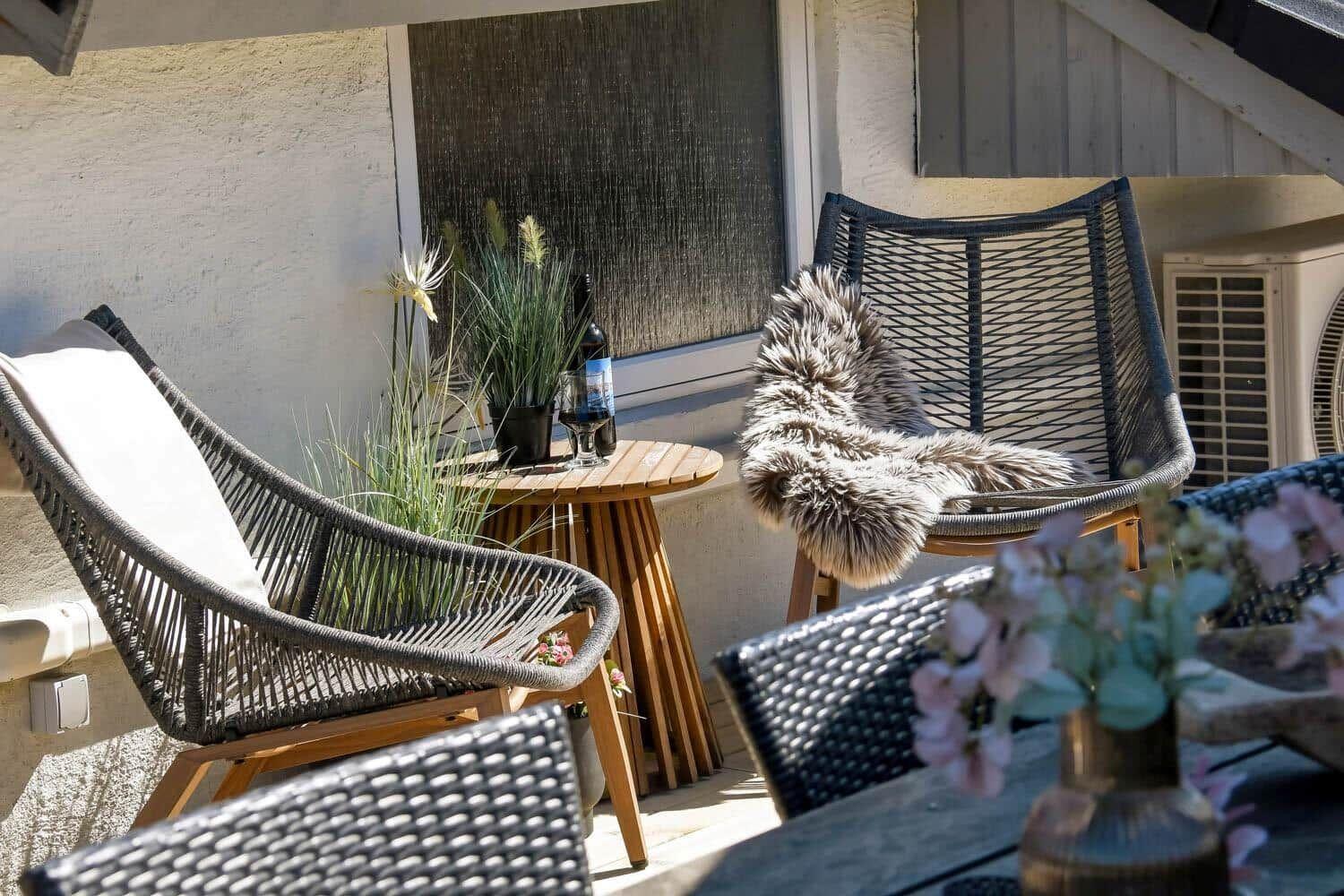 Terrasse mit zwei Stühlen, Tisch und Pflanzen. Ein Fell liegt auf einem Stuhl.