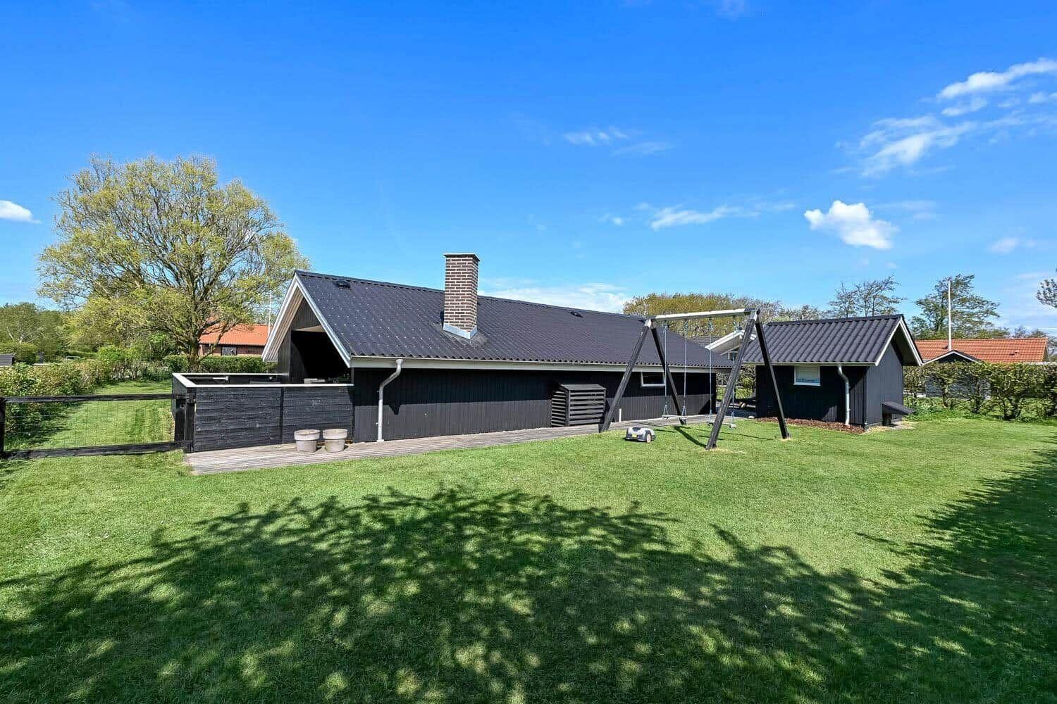Schwarzes Haus mit Garten und Schaukel unter blauem Himmel.