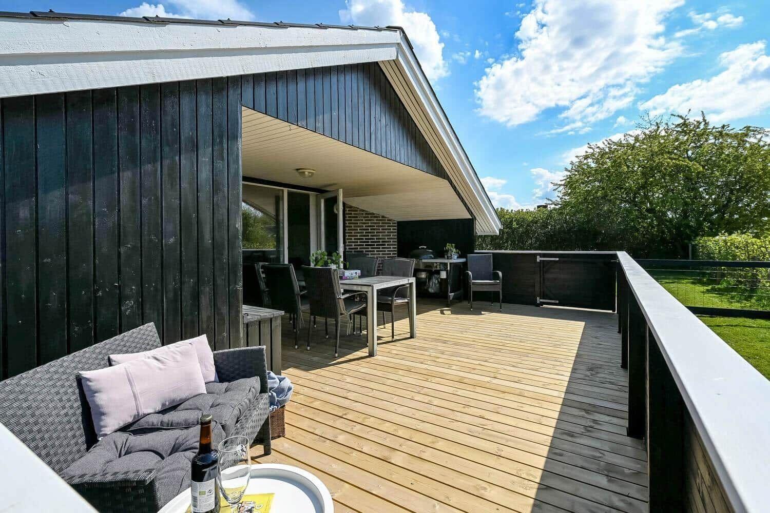 Terrasse mit Sitzgruppe, Tisch und Grill. Holzdecke, Garten und Himmel.