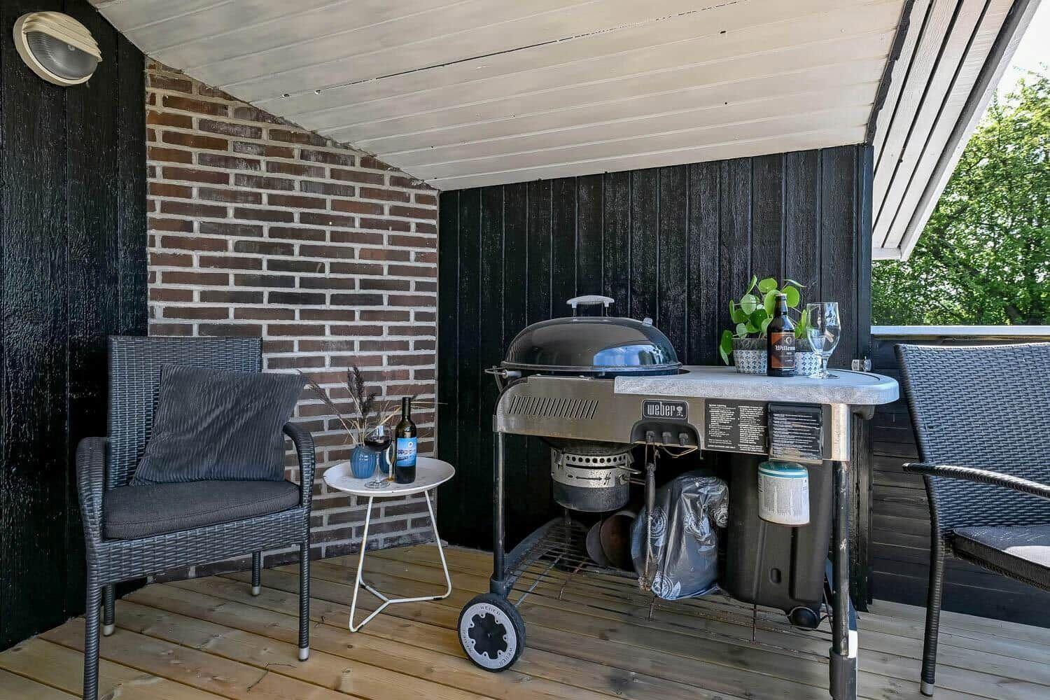 Terrasse mit Grill, Stühlen und Tisch. Holzdecke, Ziegelwand und Pflanzen.
