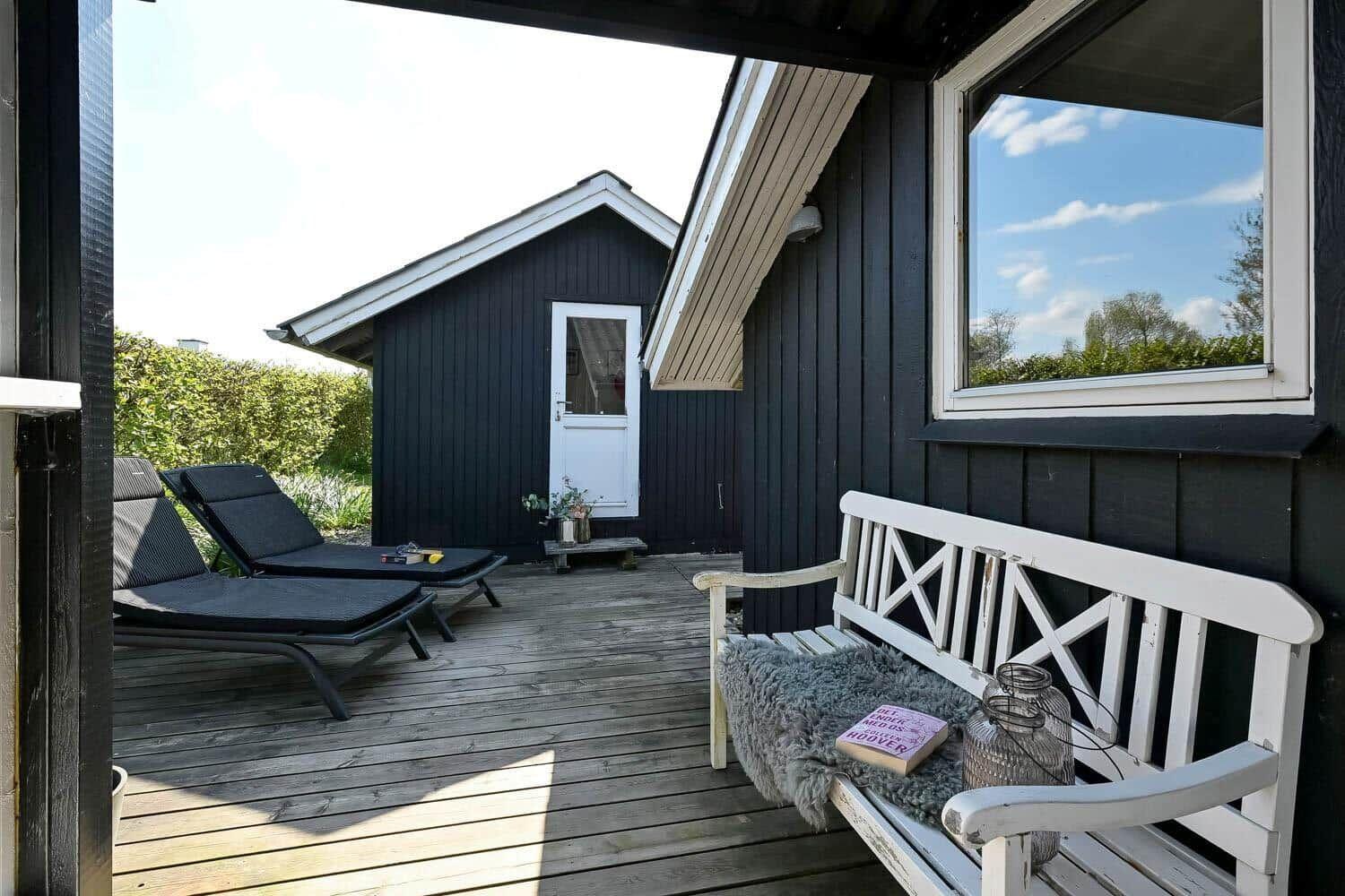 Terrasse mit Liegestühlen und weißer Bank vor einem schwarzen Holzhaus.