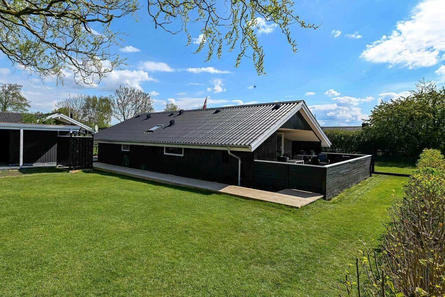 Schwarzes Haus mit Terrasse und grünem Garten unter blauem Himmel.