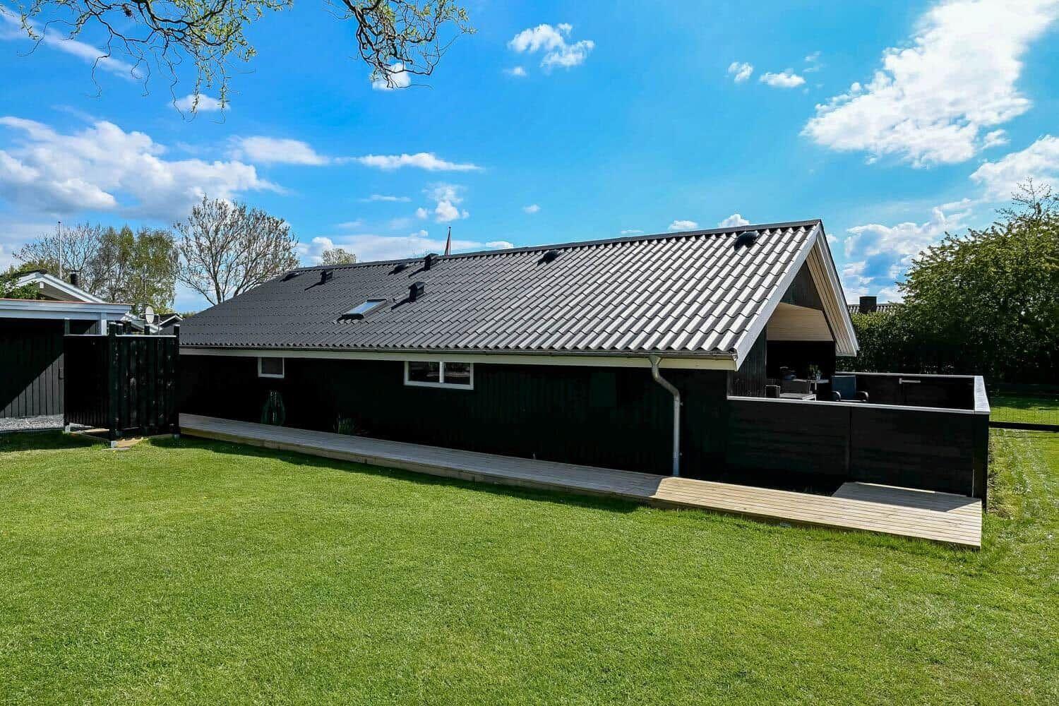 Schwarzes Haus mit Holzterrasse und grünem Rasen unter blauem Himmel.