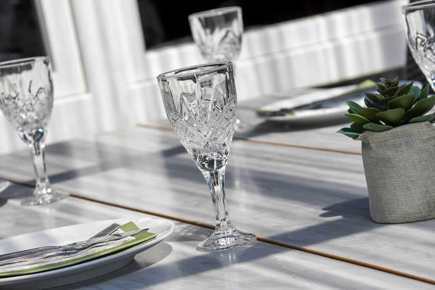 Glas, Teller und Besteck auf einer Terrasse mit Pflanze.