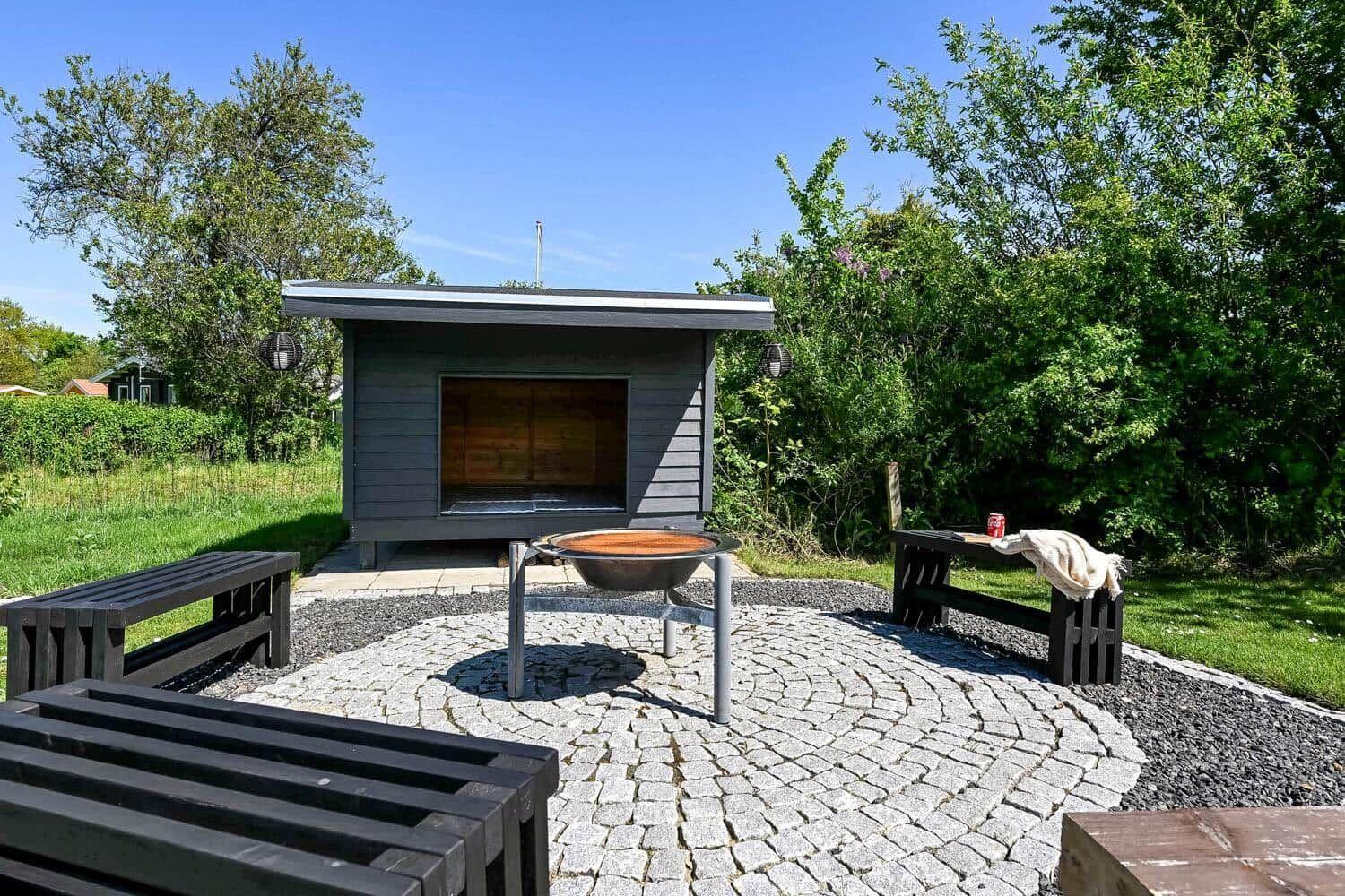 Außenbereich mit Sauna, Grill und Bänken auf Steinplatten.