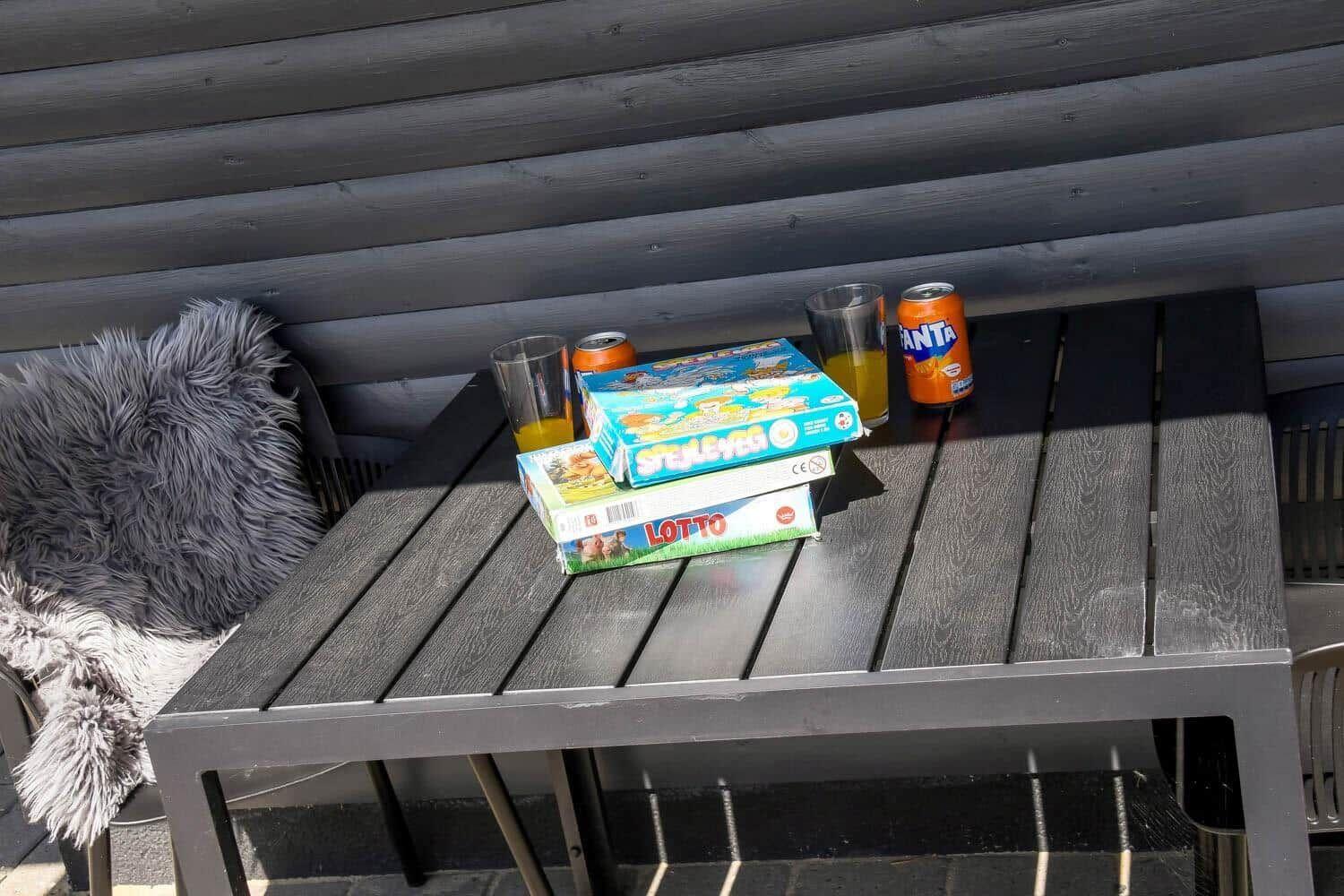 Tisch mit Spielen, Getränken und Fellkissen unter einer Holzveranda.