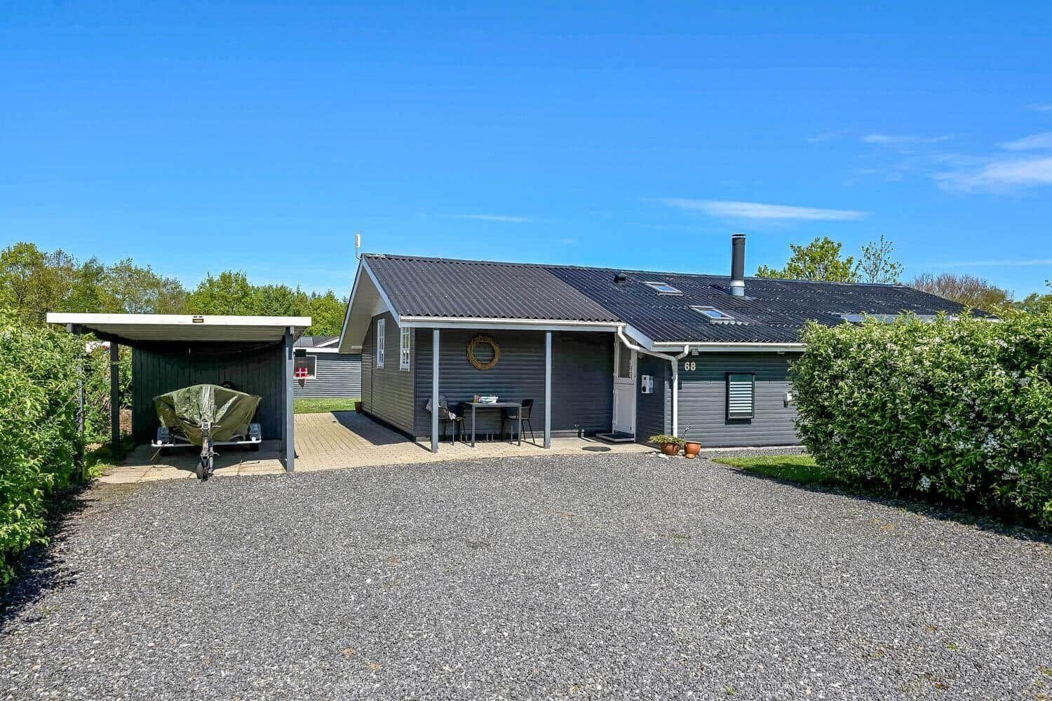 Ein graues Ferienhaus mit Terrasse, Grillplatz und Garage für Boot.