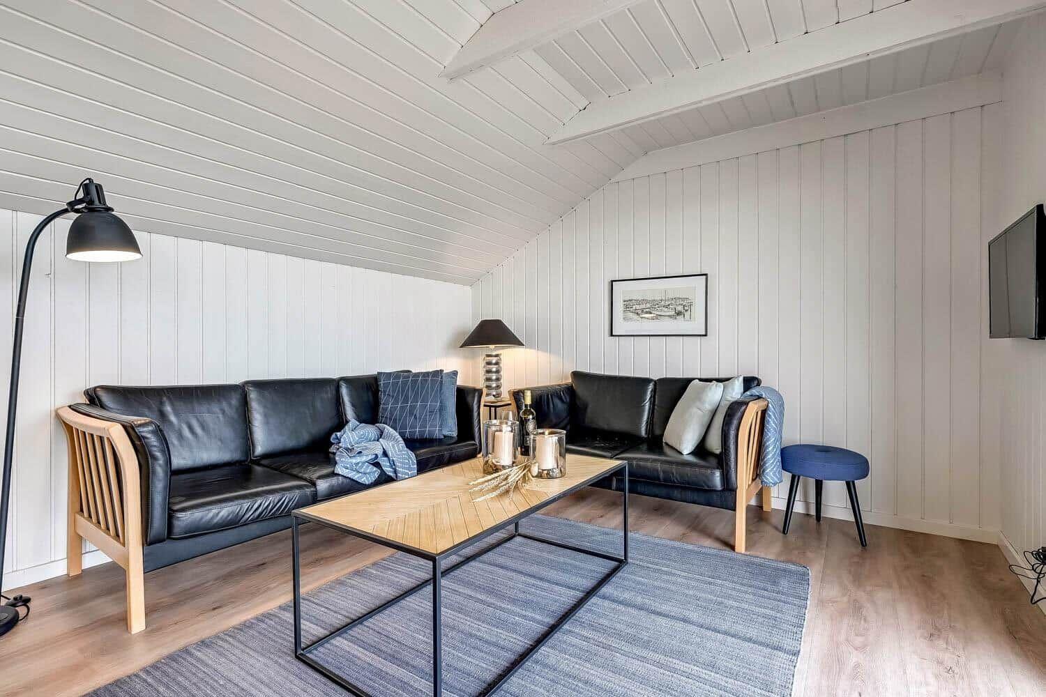 Wohnzimmer mit zwei schwarzen Ledersofas, Holztisch und TV.