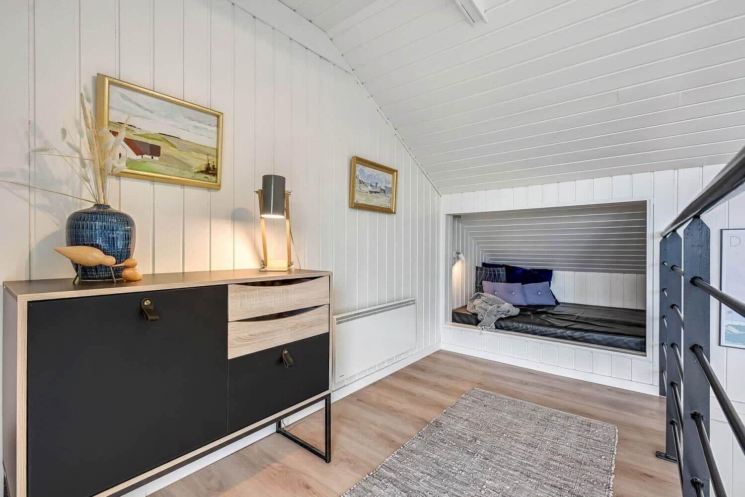 Schlafzimmer mit Nische, Schrank und Wandbildern. Holzboden und weiße Wände.