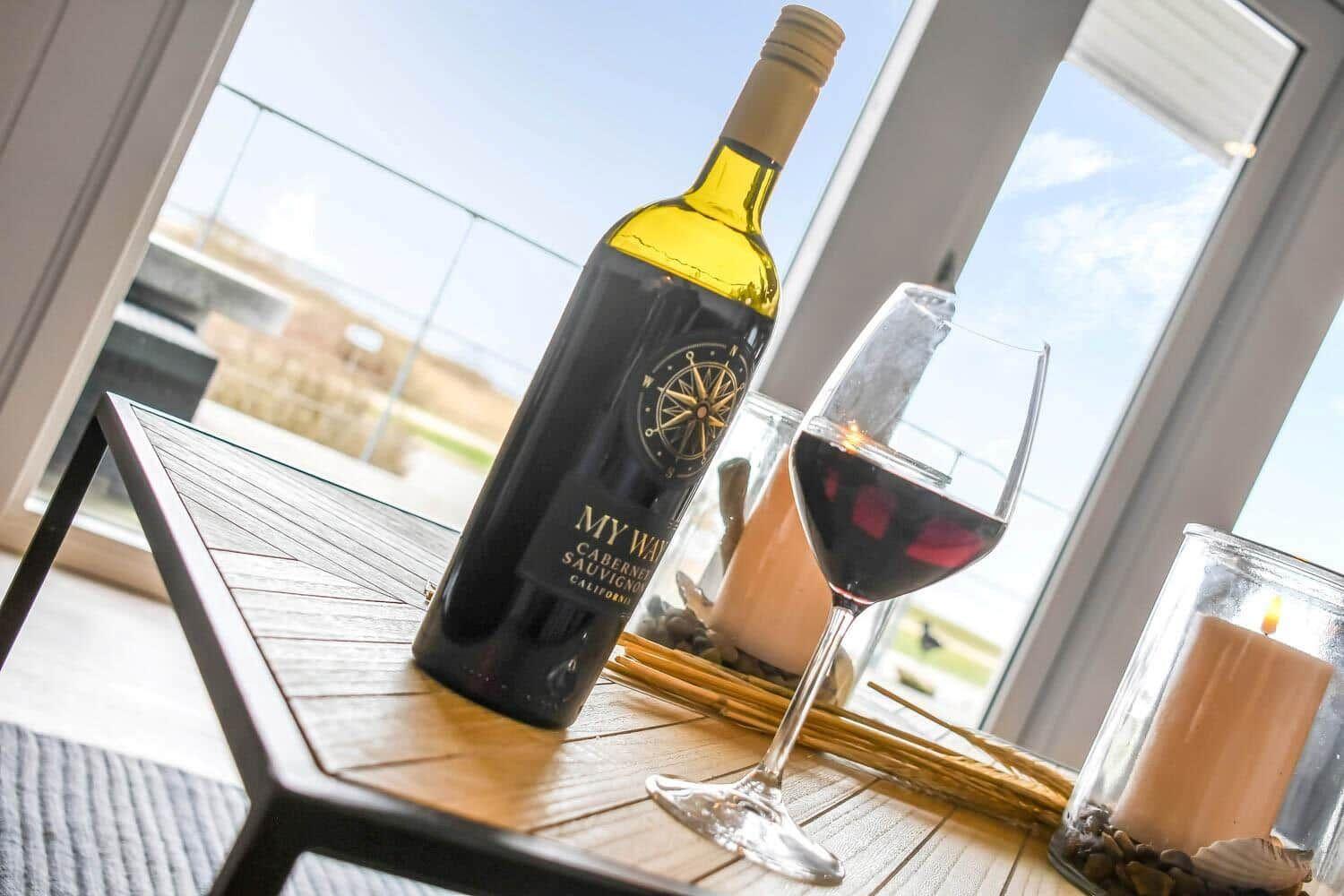 Eine Flasche Wein und ein Glas stehen auf einem Tisch vor einem Fenster.