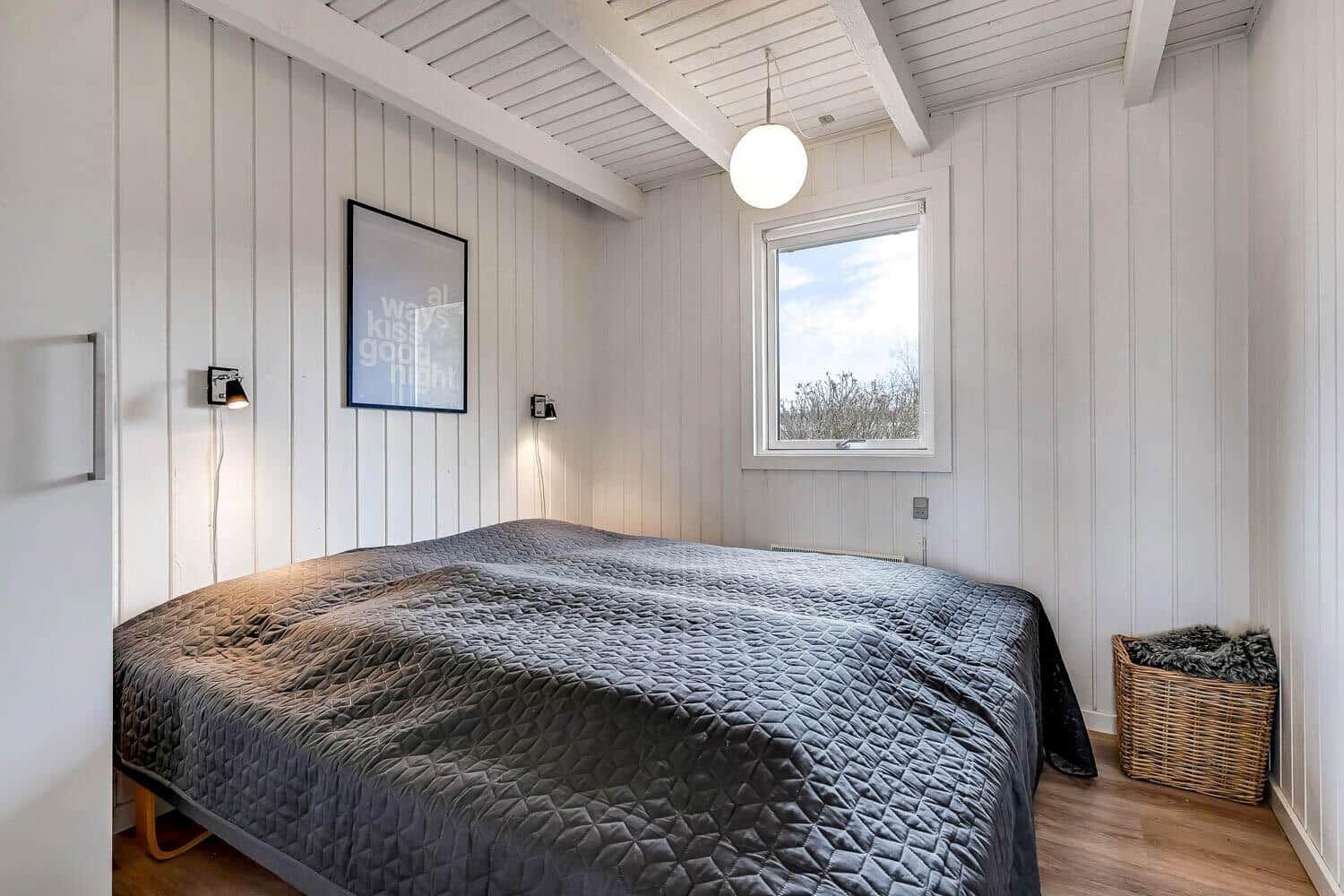 Schlafzimmer mit Bett, Wandbild und Fenster. Holzdecke und Wandpaneelen.