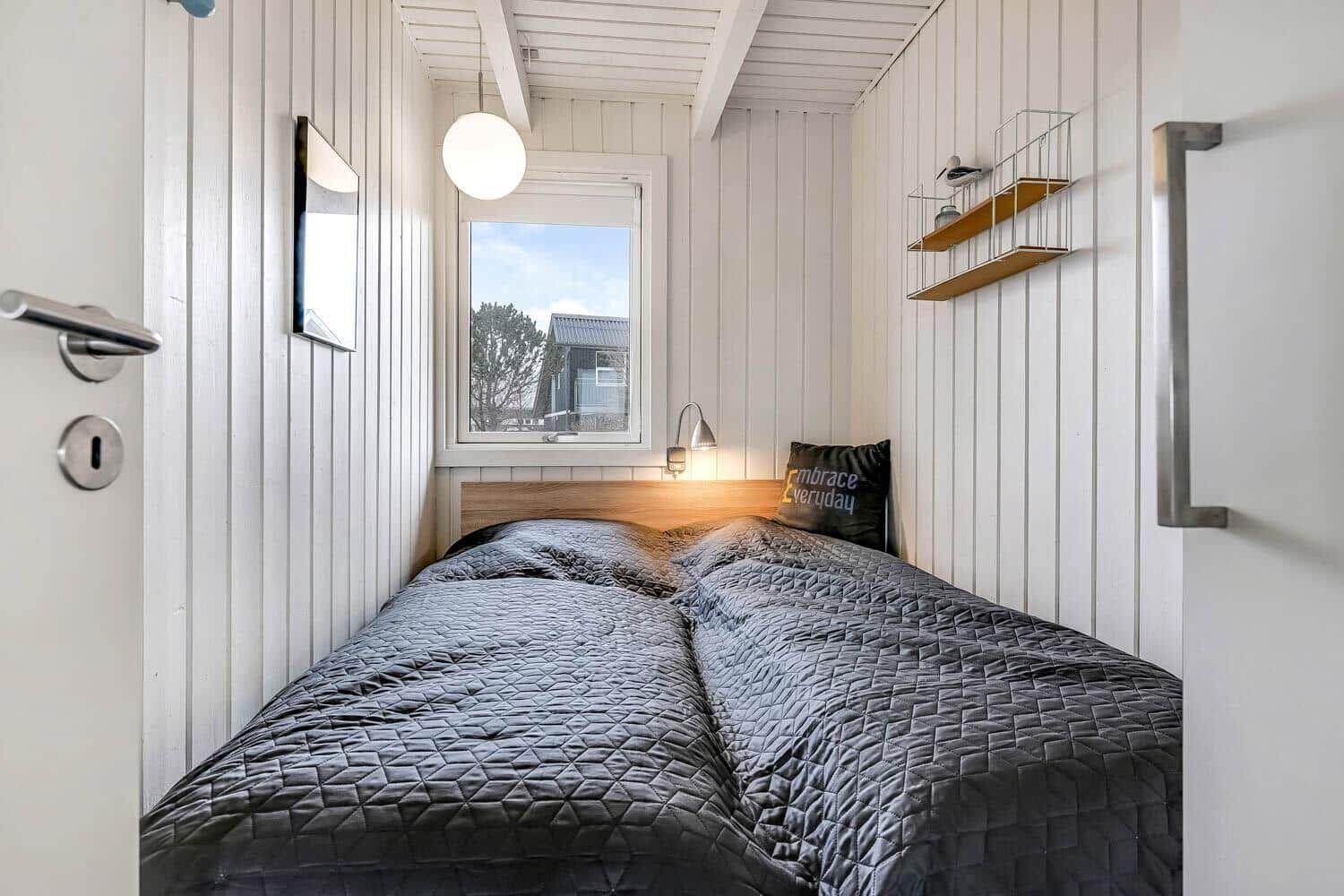 Schlafzimmer mit Bett, Fenster und Wandregal.