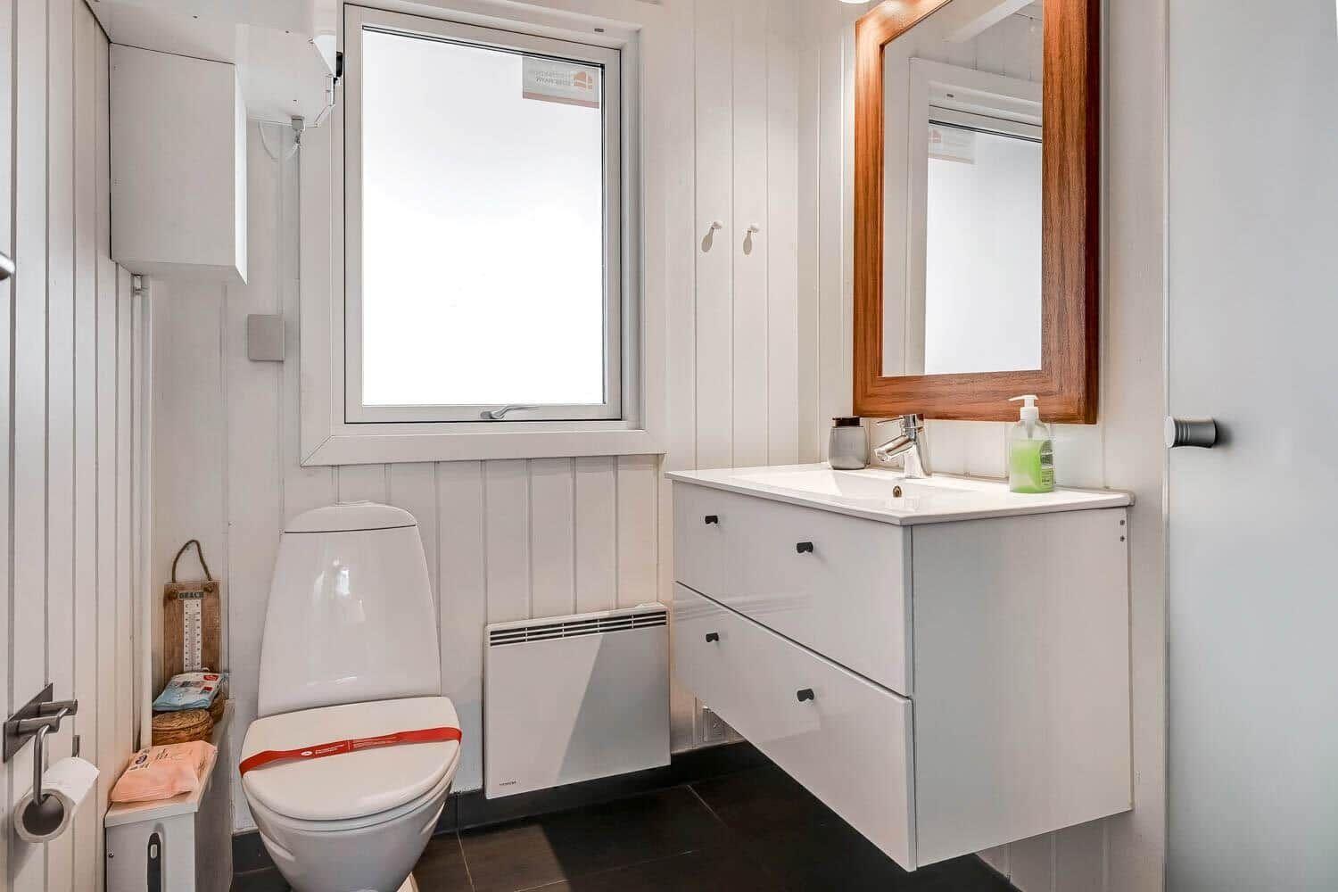 Badezimmer mit Toilette, Waschbecken und Fenster. Holzrahmen Spiegel und Heizkörper.