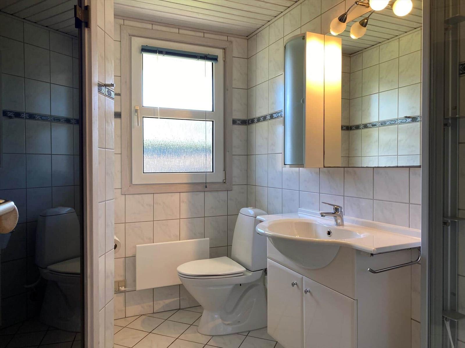 Badezimmer mit Toilette, Waschbecken und Dusche. Fenster mit Rollladen und Spiegelschrank.