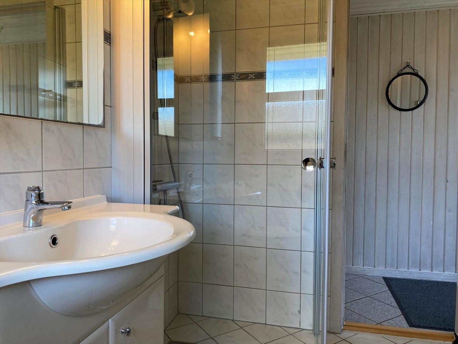 Badezimmer mit Dusche, Waschbecken und Spiegel an der Wand.
