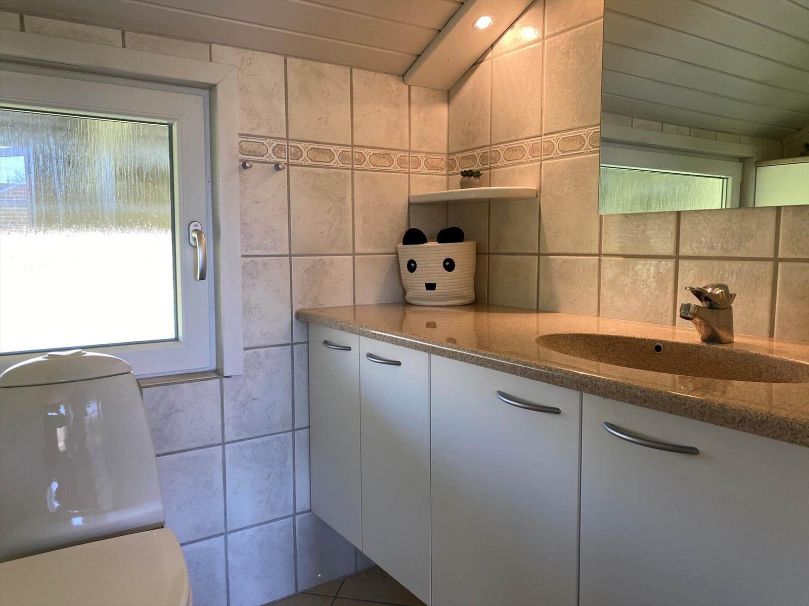 Badezimmer mit Waschbecken, Spiegel und Fenster. Auf der Arbeitsplatte steht eine Schale mit Panda-Motiv.