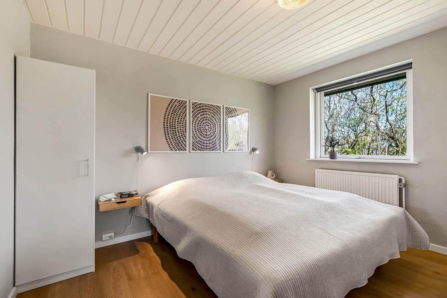 Schlafzimmer mit Doppelbett, Fenster und Kleiderschrank. Decke mit Holzverkleidung.