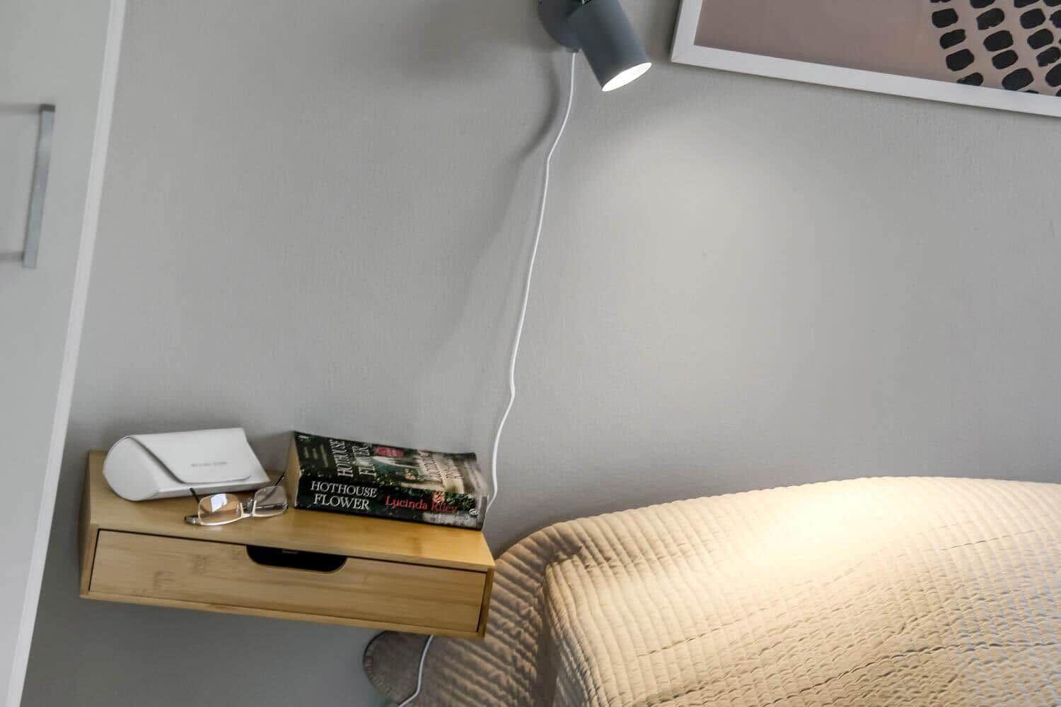 Schlafzimmer mit Nachttisch, Buch und Wandlampe.