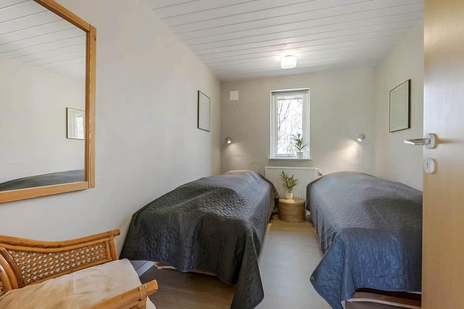 Zwei Betten mit dunklen Bezügen, Spiegel, Fenster und Pflanzen in einem Raum.