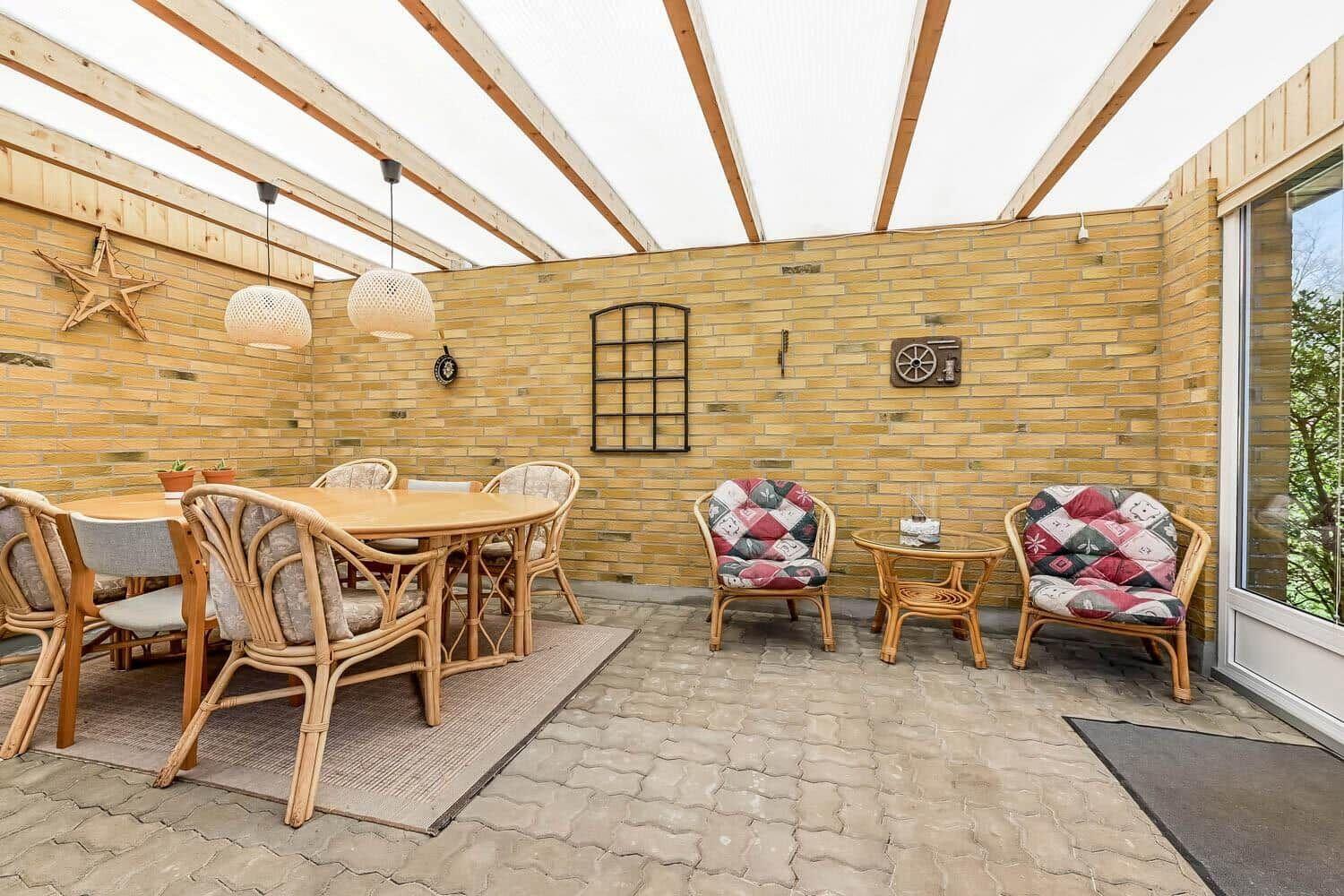 Terrasse mit Sitzgruppe, Esstisch und Holzwand. Überdacht mit Holzrahmen und weißen Lampen.
