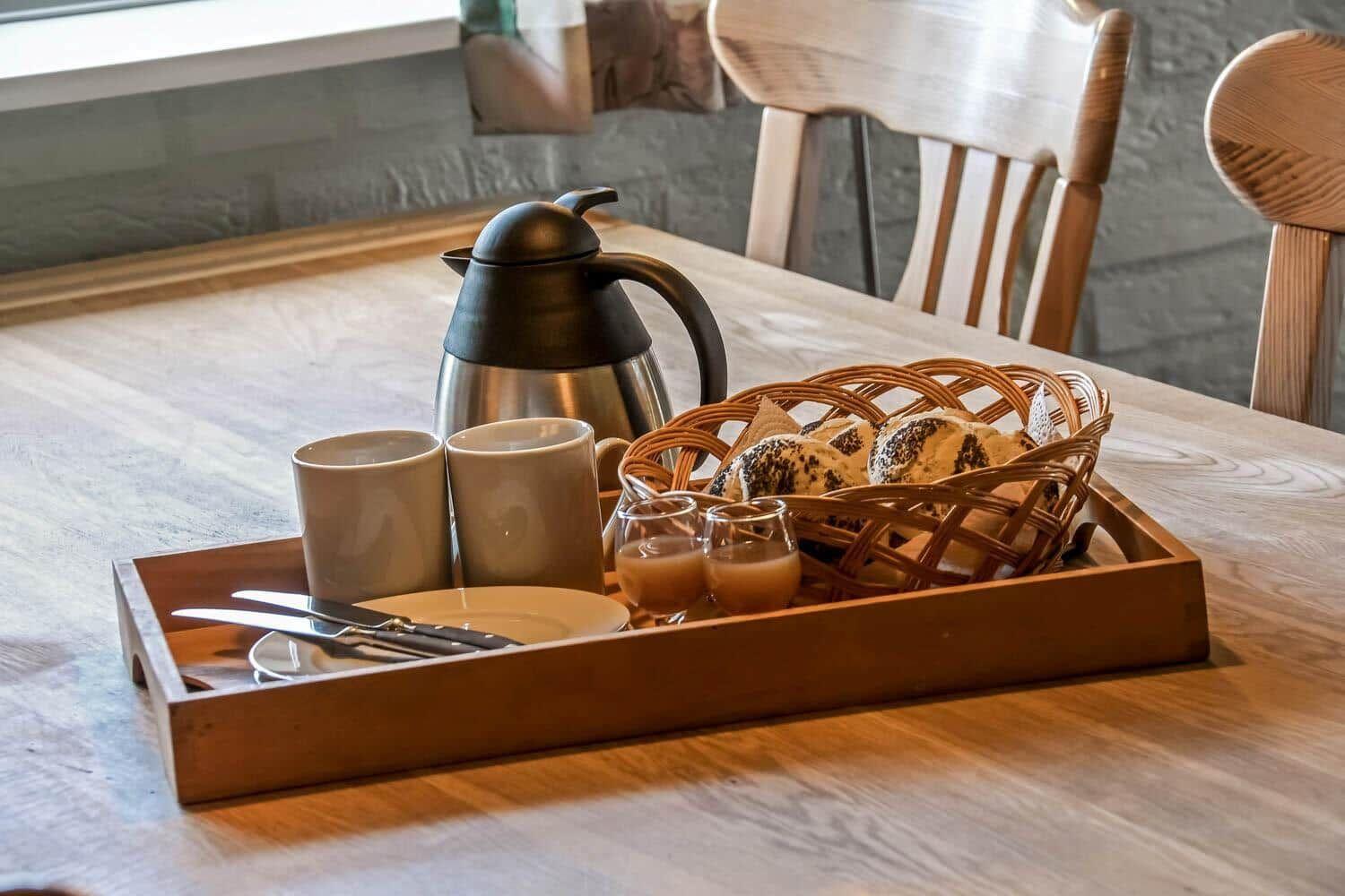 Frühstückstablett mit Kaffee, Brot und Gläsern auf Holztisch