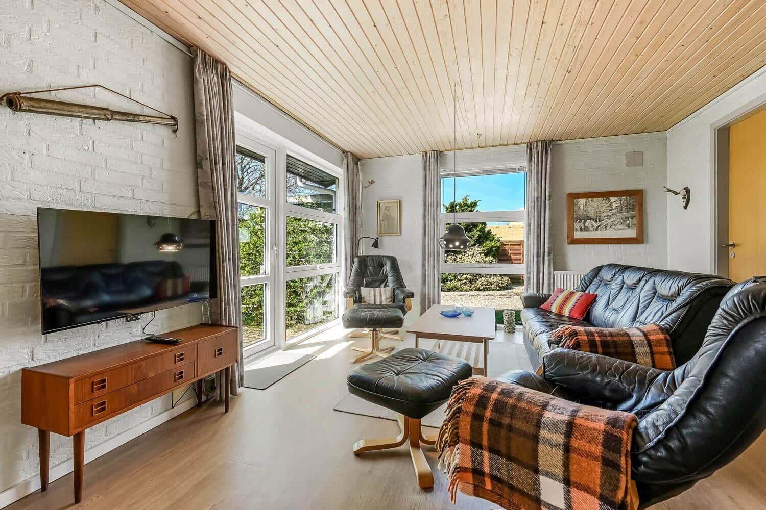 Wohnzimmer mit Ledersofa, Fernseher und großen Fenstern.