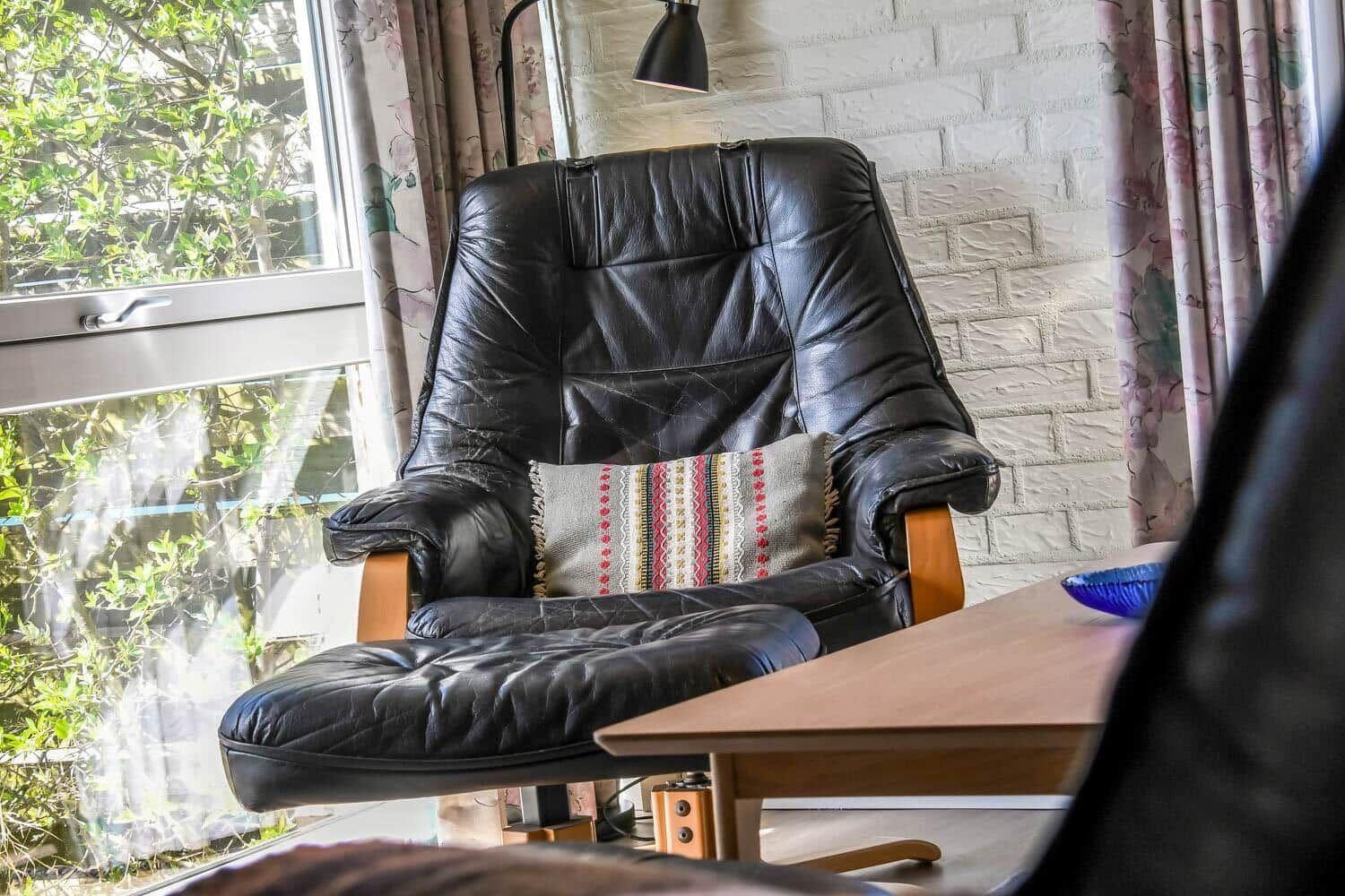 Schwarze Ledersessel mit Kissen vor Fenster mit Blick auf grüne Pflanzen.