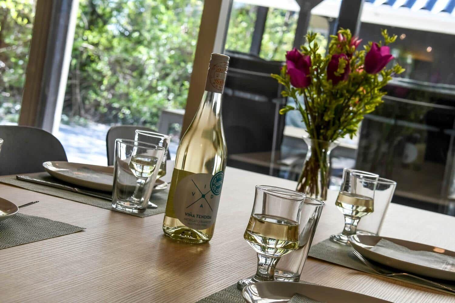 Gedeckter Tisch mit Weinflasche und Gläsern, Blumenstrauß und Blick auf Garten.