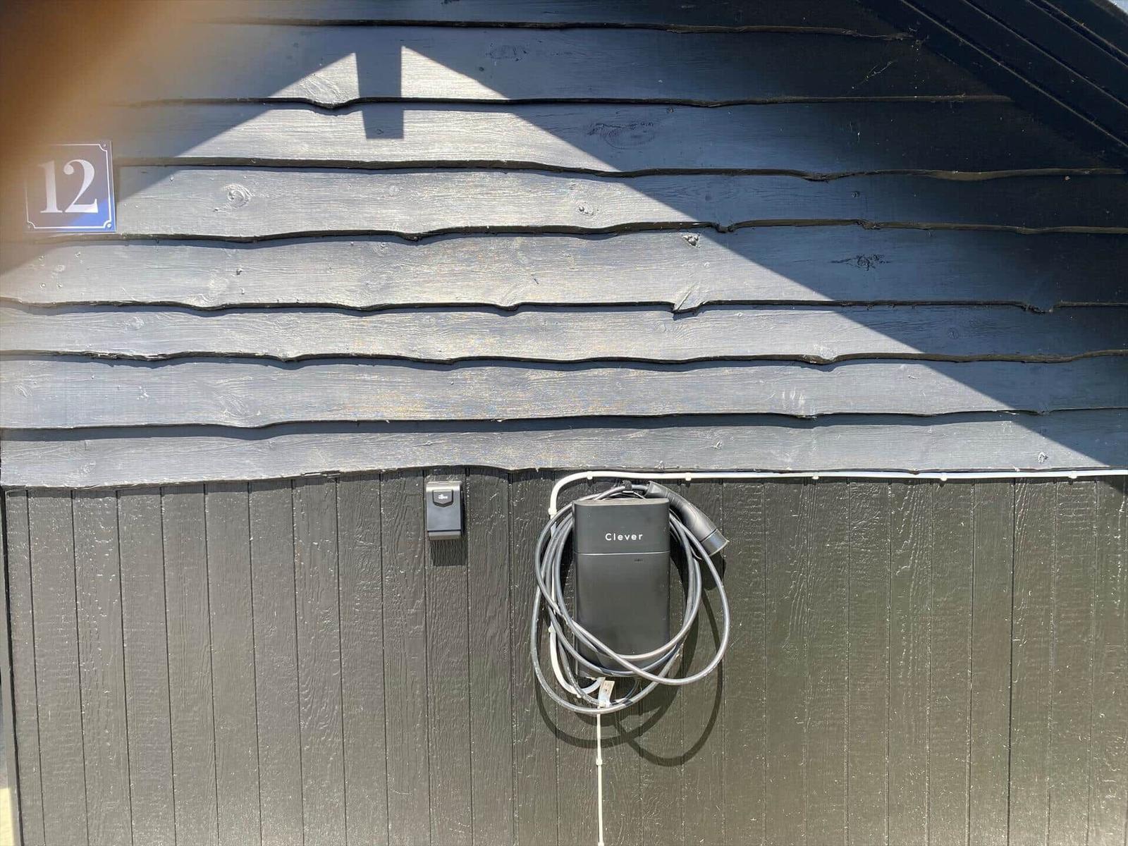 Außenansicht einer Hauswand mit Elektroauto-Ladestation und Hausnummer 12.
