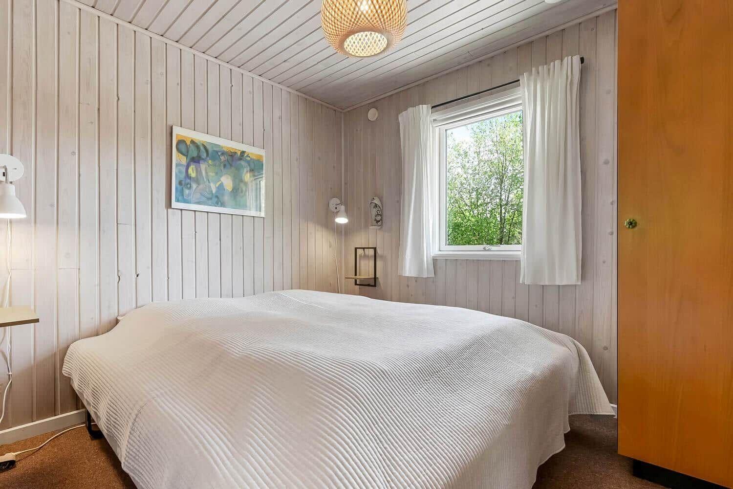 Schlafzimmer mit Bett, Fenster und Holzwandverkleidung.