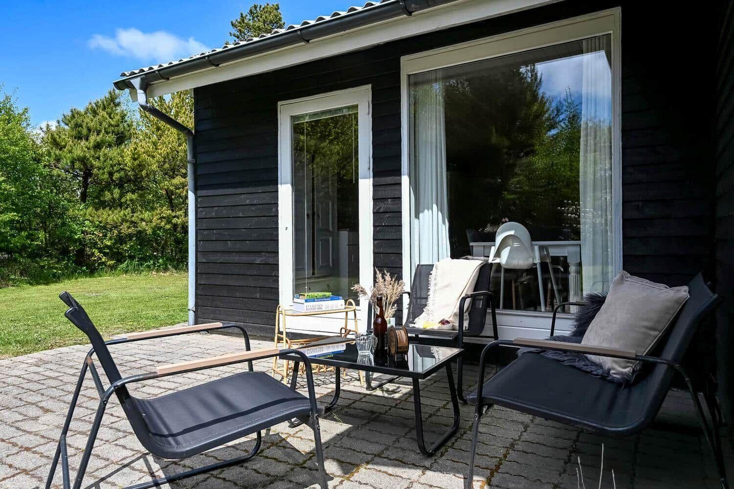 Terrasse mit zwei Stühlen und Tisch vor einem Haus mit großen Fenstern.