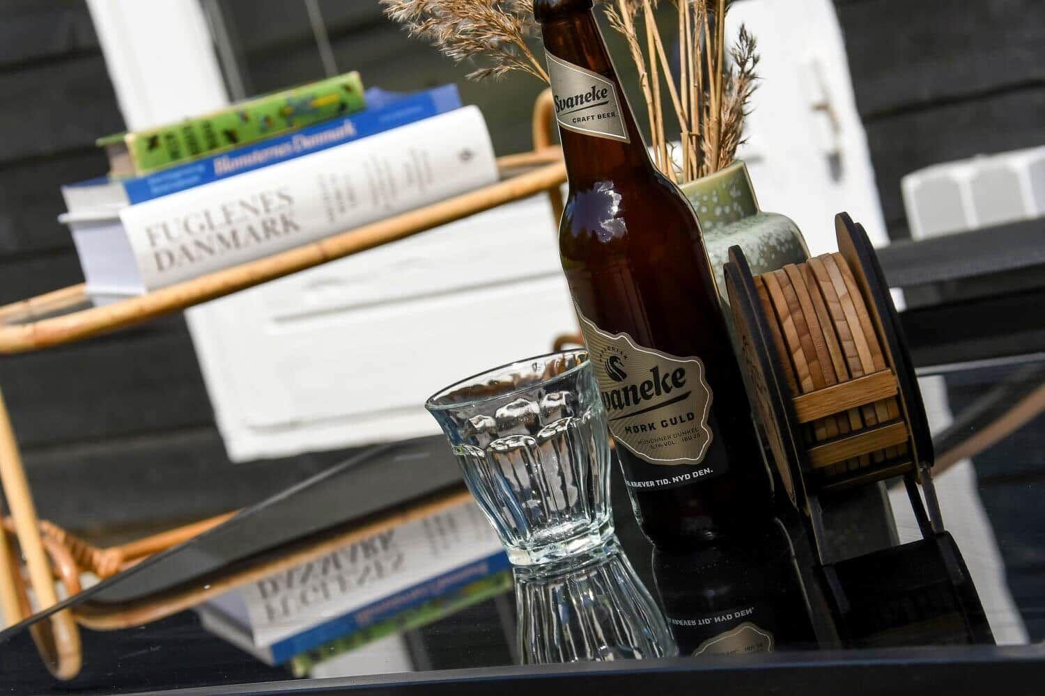 Eine Flasche Bier und ein Glas stehen auf einem Tisch mit Büchern und einem Holztablett.